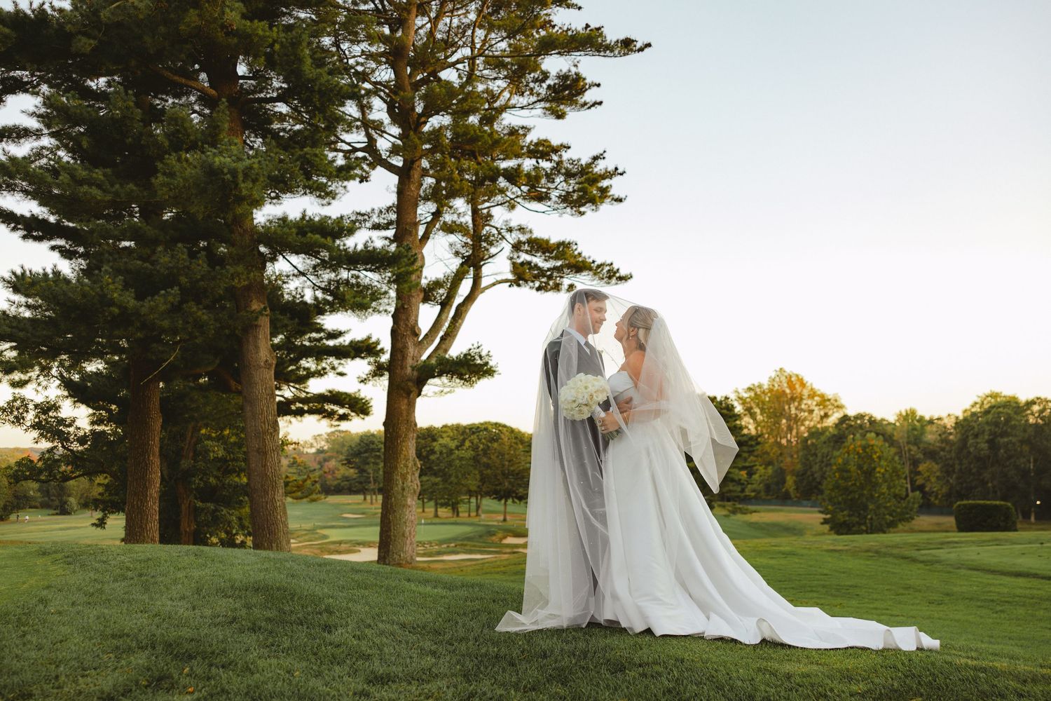Bride and groom share a romantic moment on a lush golf course at golden hour.