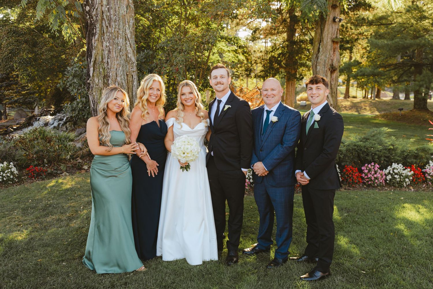 Bride and groom pose with family members outdoors in garden setting on their wedding day.