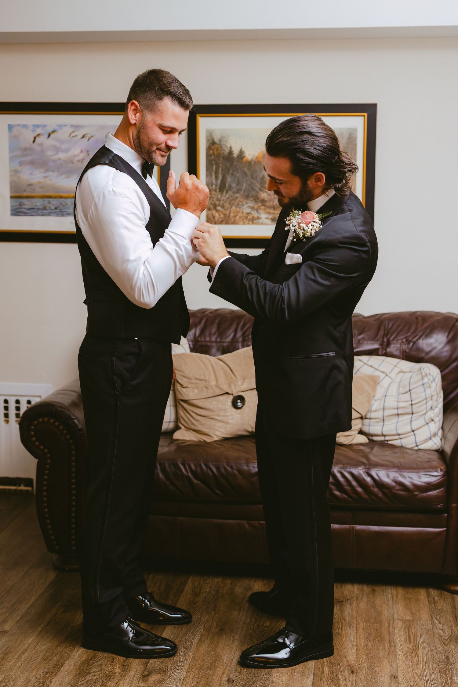 Groomsman helping groom with cufflinks in a cozy room with leather sofa before the wedding.
