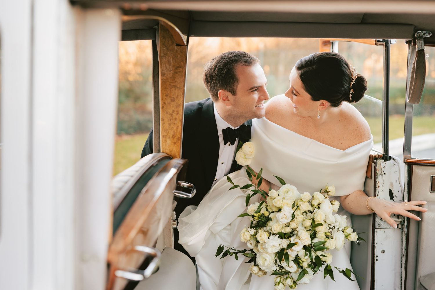 Bride and groom leaning in for a kiss inside a classic vintage automobile.