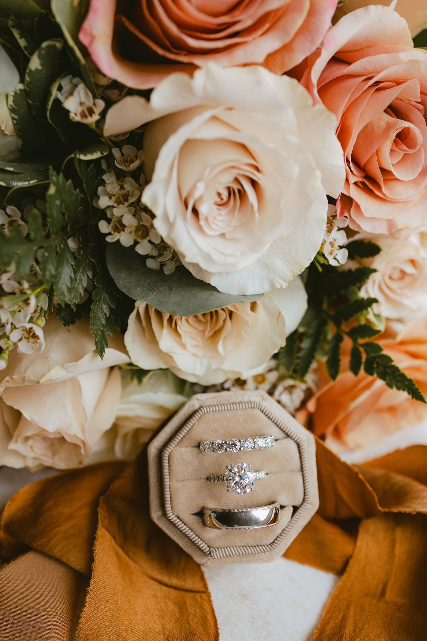 Diamond engagement ring and wedding bands in velvet box surrounded by pink and cream roses.