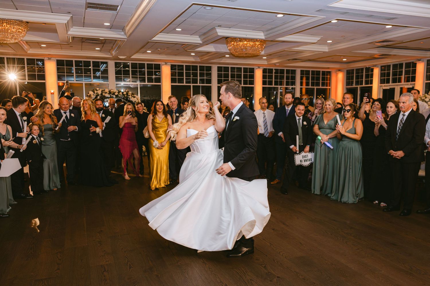 Bride twirls in white gown during first dance as guests watch in elegant wedding reception venue.