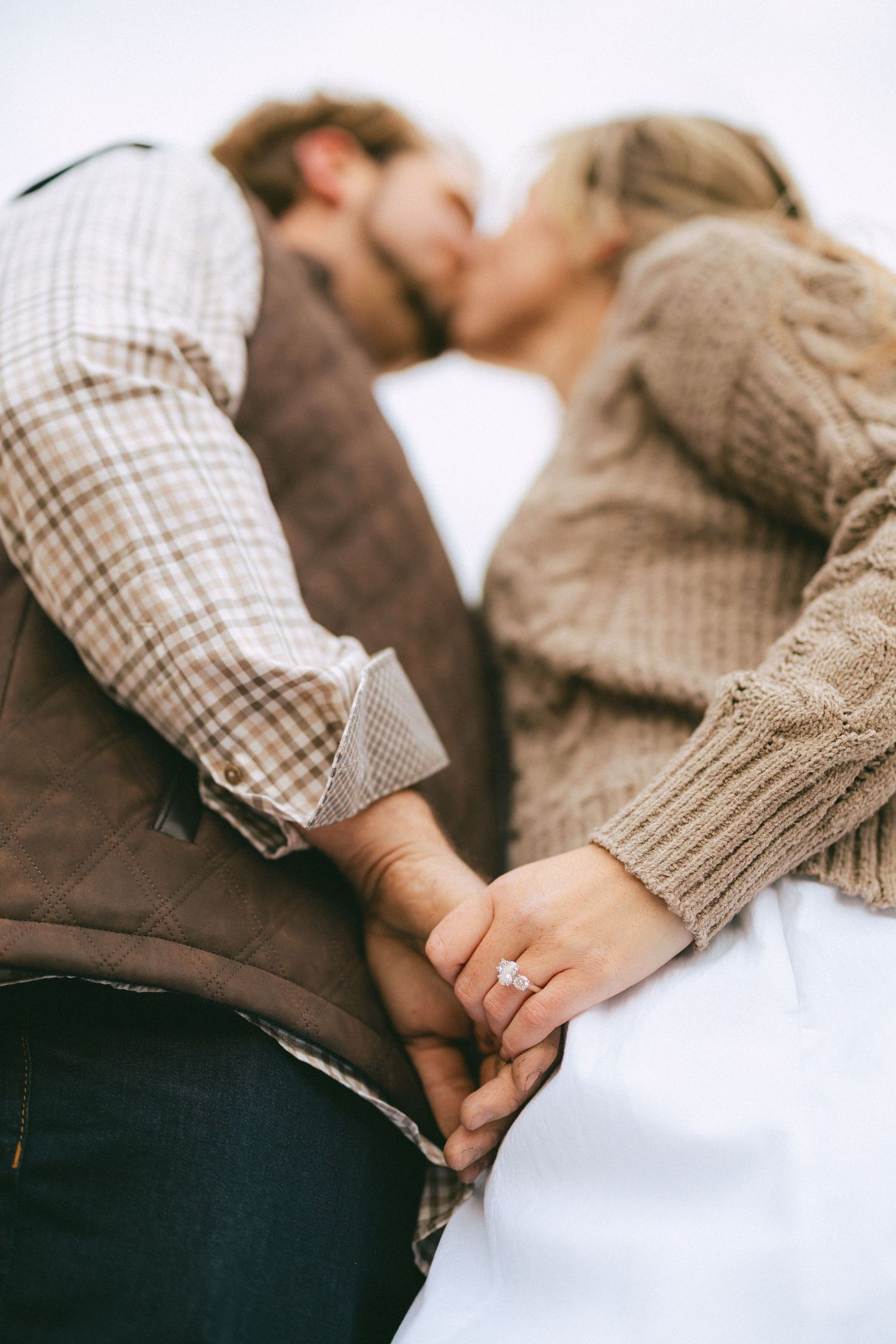 Close-up of engaged couple kissing while holding hands, showcasing diamond engagement ring, in fall outfits.