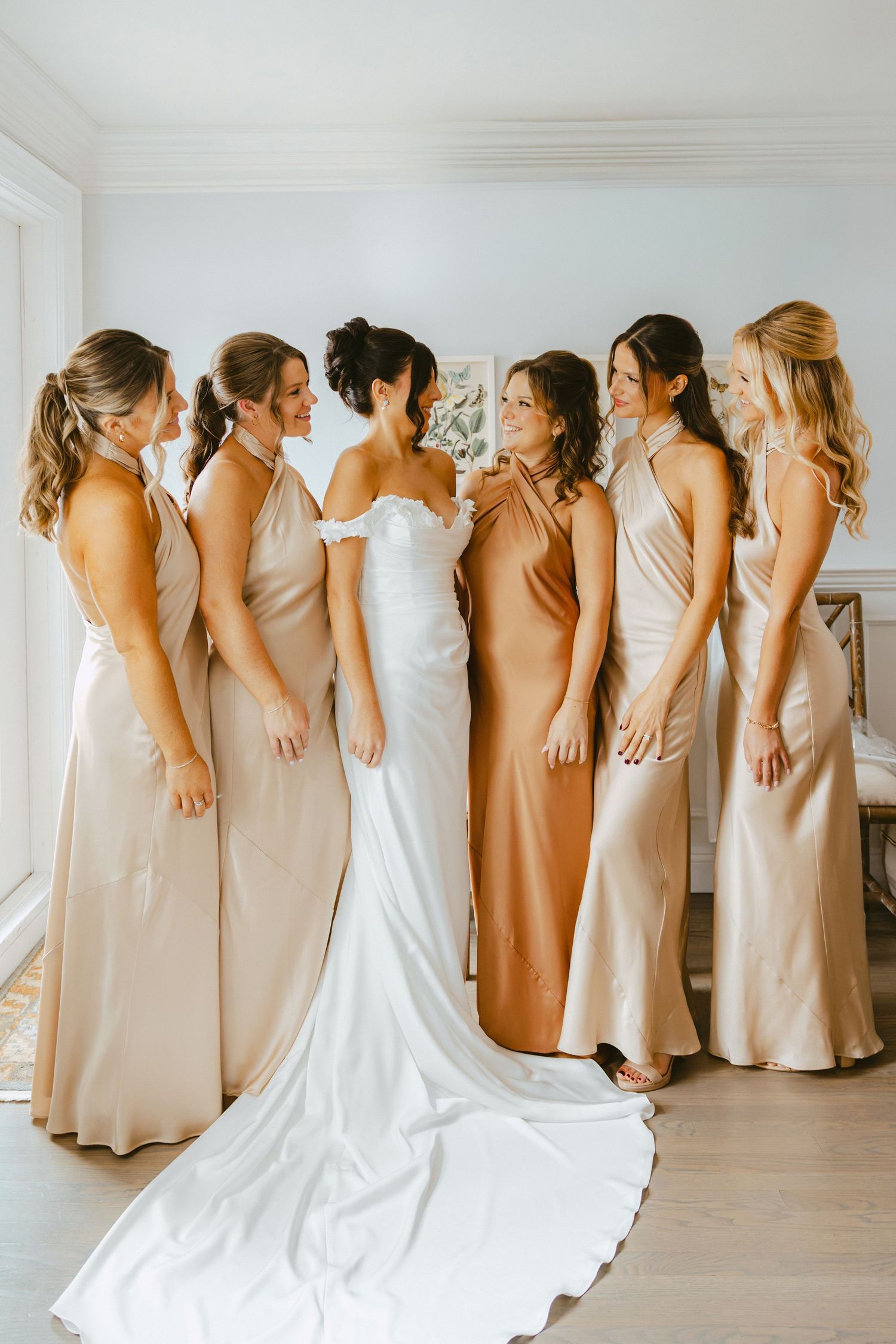 Bride in off-shoulder gown surrounded by five bridesmaids in champagne and gold satin dresses.