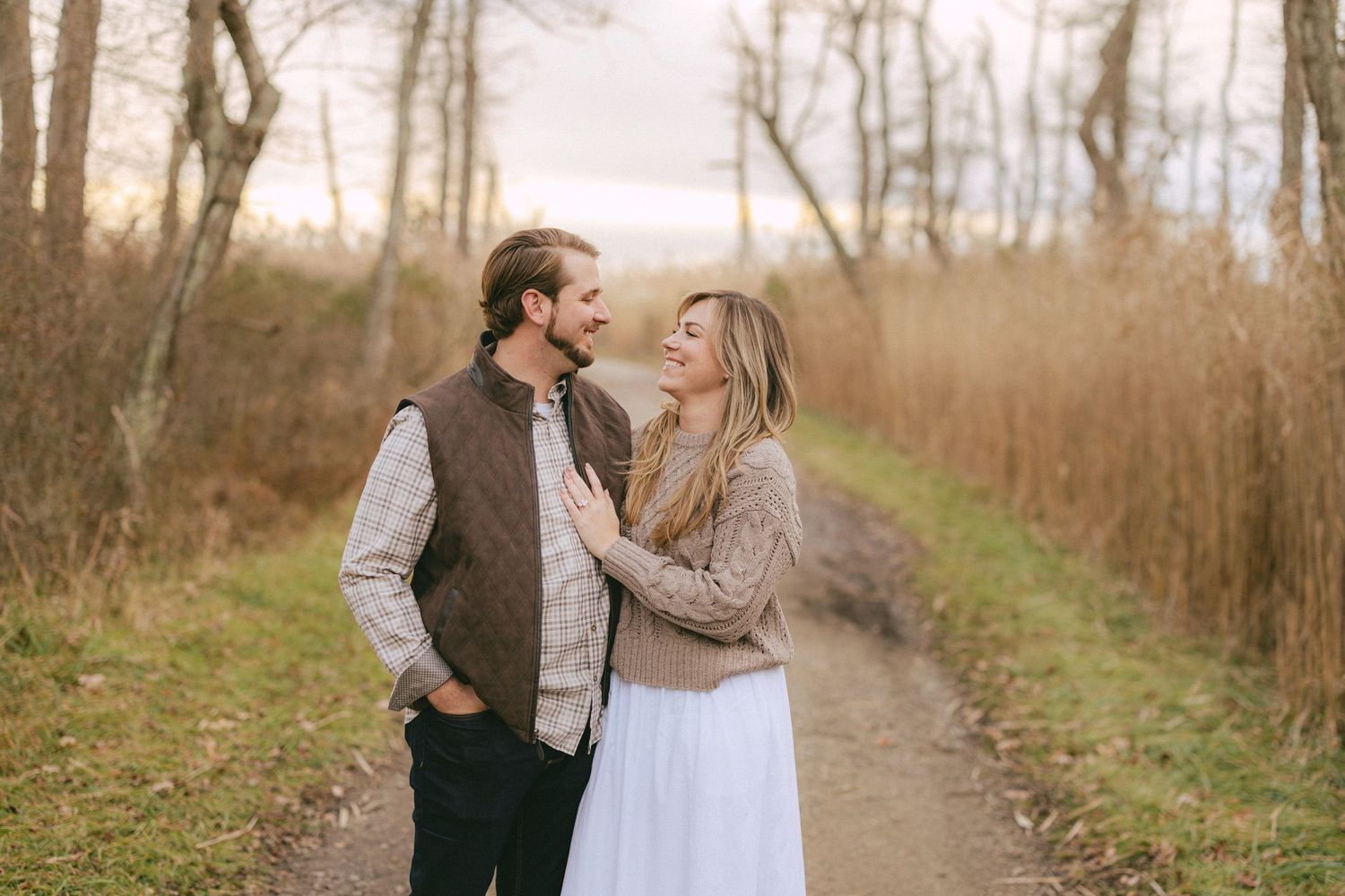 Laughing couple standing together on a gravel path surrounded by tall golden grasses in fall.