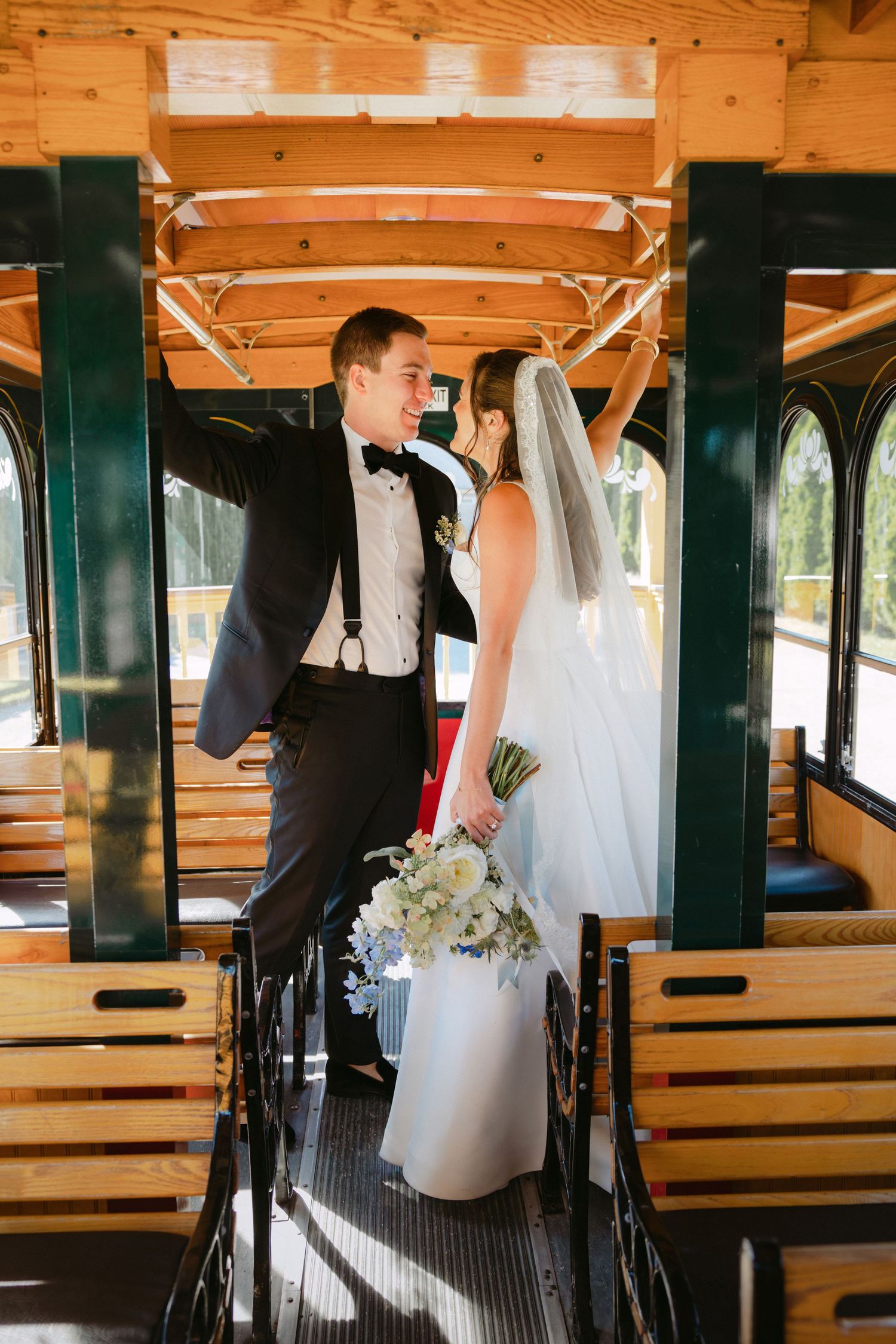 Bride and groom share a joyful moment inside a vintage wooden trolley car after wedding.