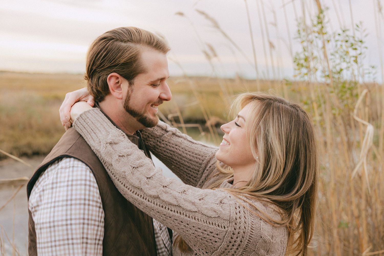 Woman with arms around a mans neck smiling lovingly at him in a sunlit grassy field.