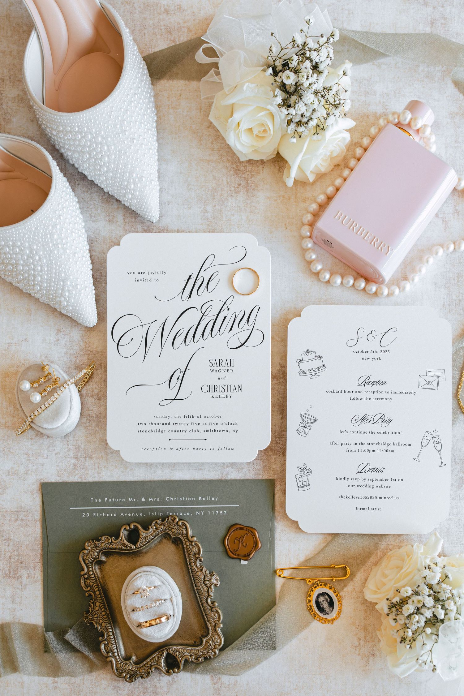Elegant wedding flat lay featuring invitation suite, pearl heels, rings, perfume, and floral accents.