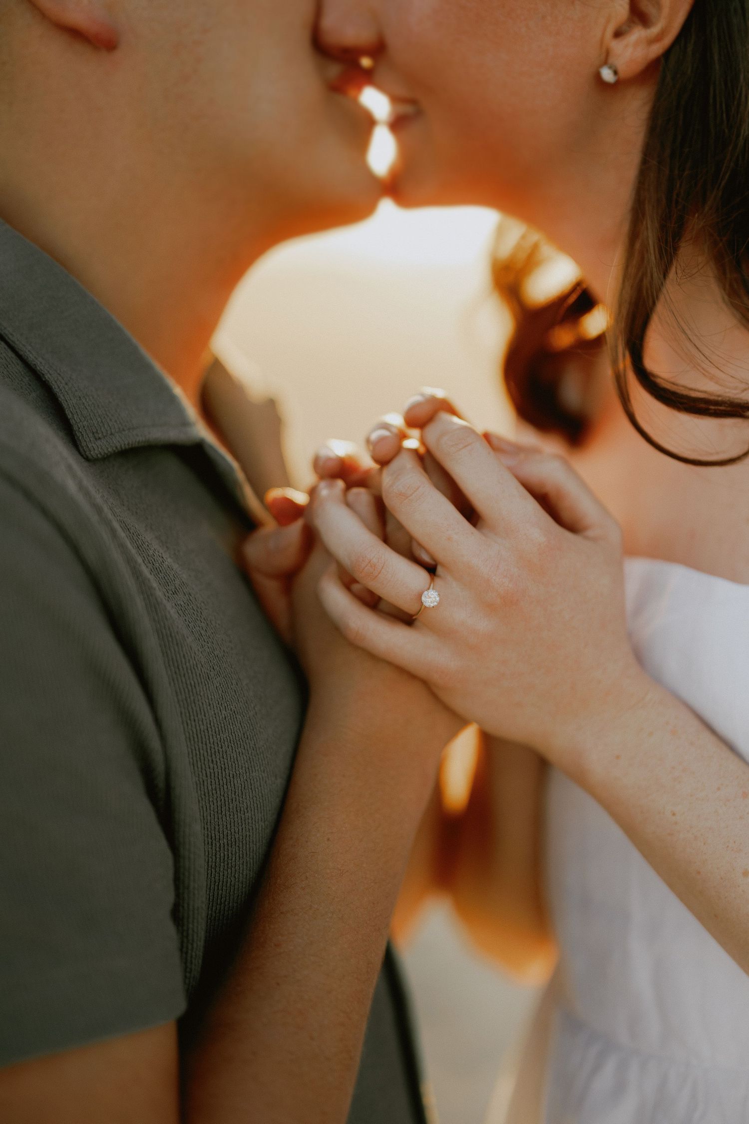 Close-up of engaged couple holding hands showing diamond engagement ring at golden sunset.