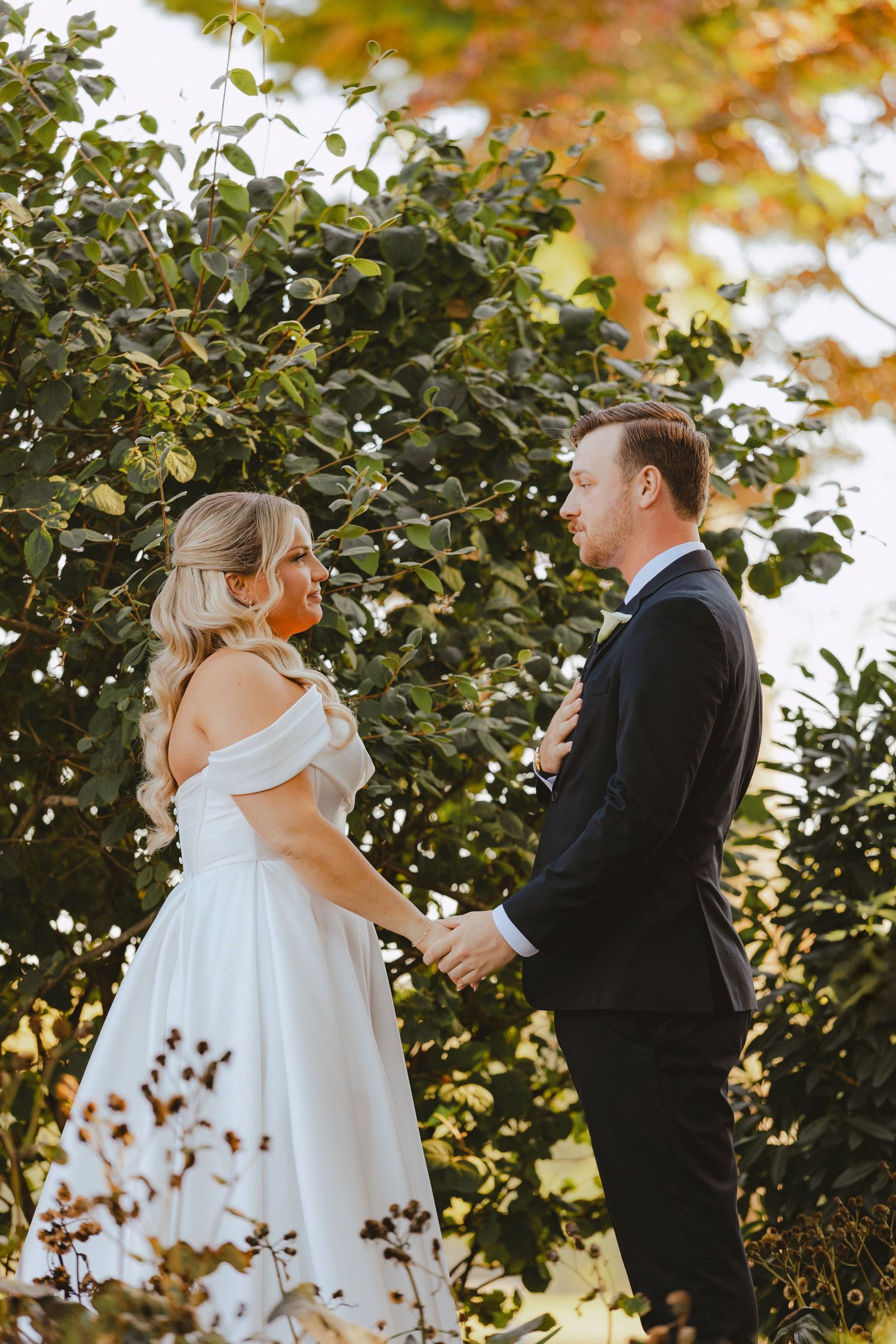 Bride and groom hold hands and share an intimate first look moment surrounded by lush greenery.