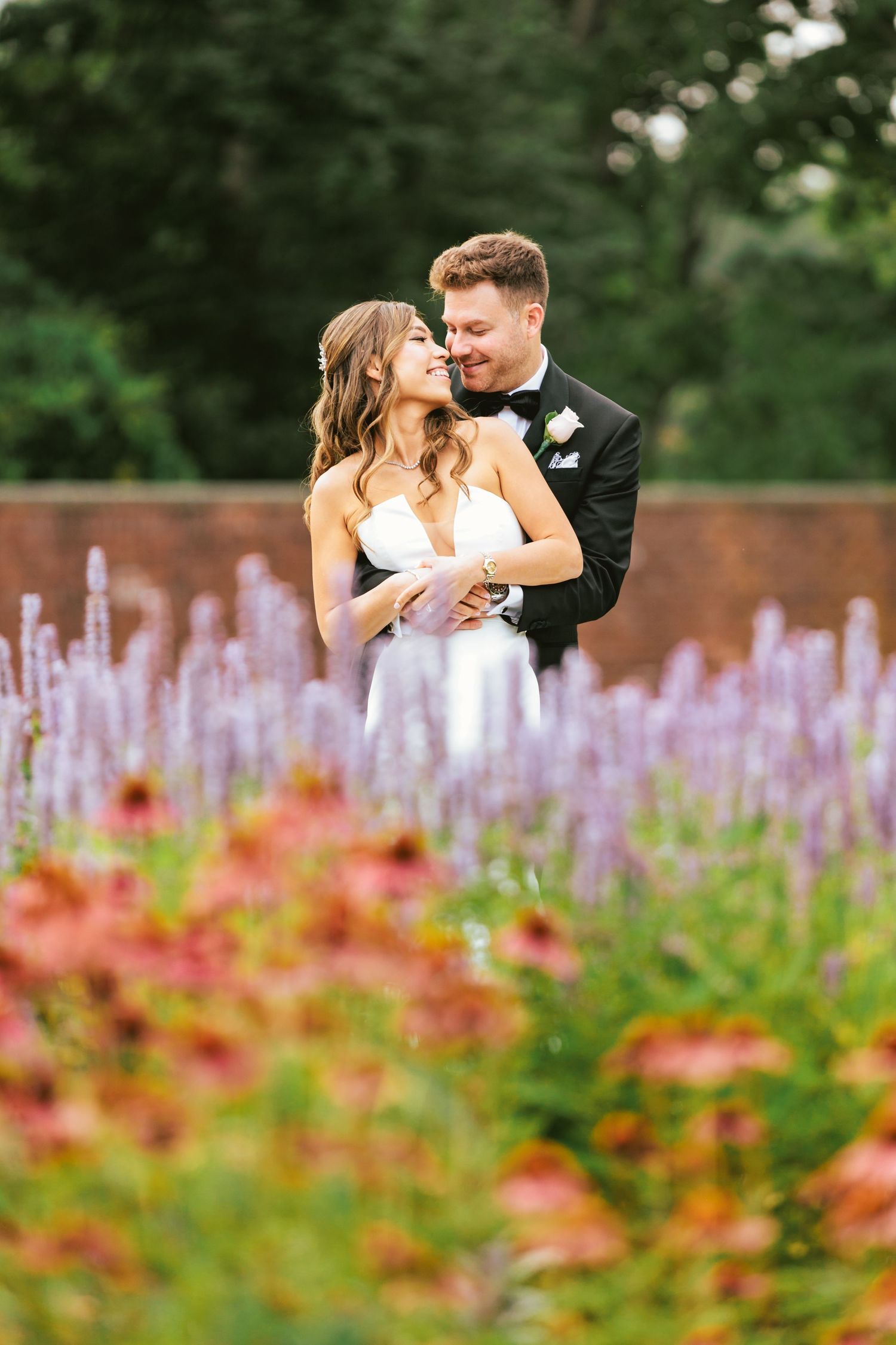Bride and groom embracing romantically in a garden surrounded by colorful wildflowers.