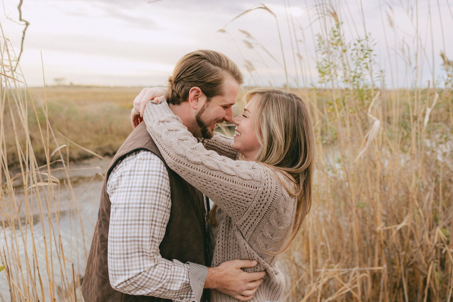 Couple sharing a romantic embrace and nearly kissing in a golden field of tall grass.