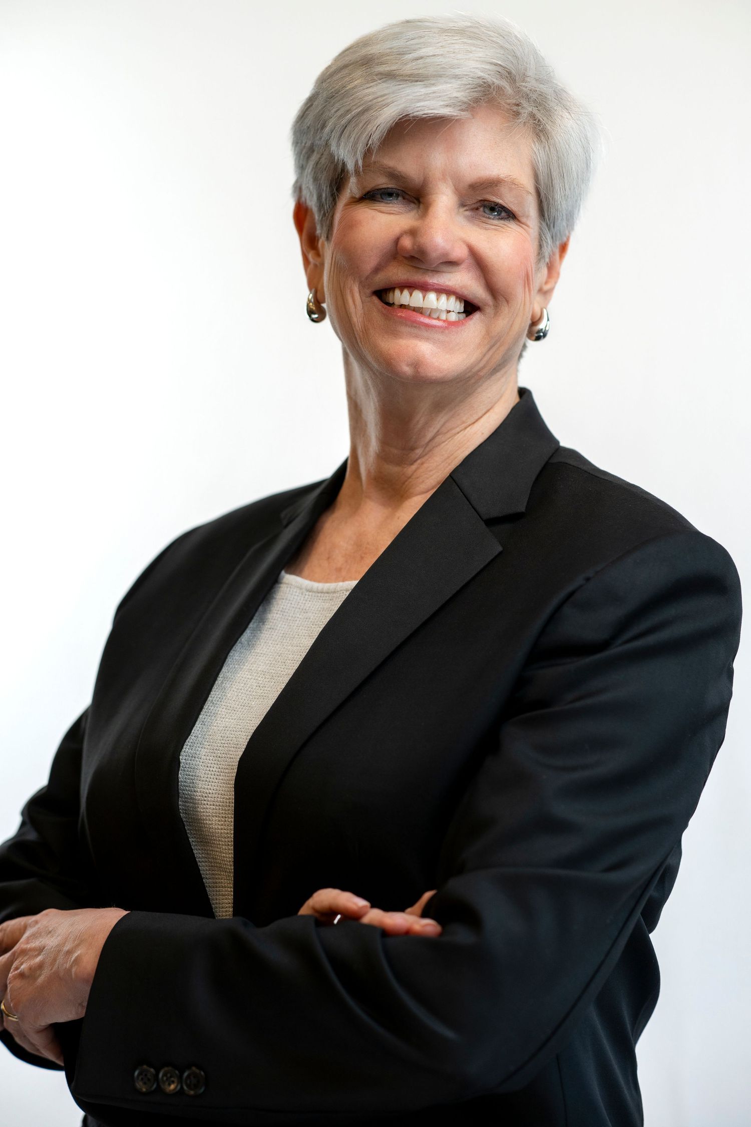 Professional woman with gray hair in black blazer smiling with arms crossed on white background. Boston Headshot Photographer