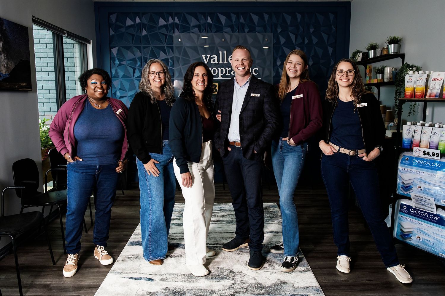 Valley Chiropractic team of six professionals smiling together in a modern clinic waiting room.