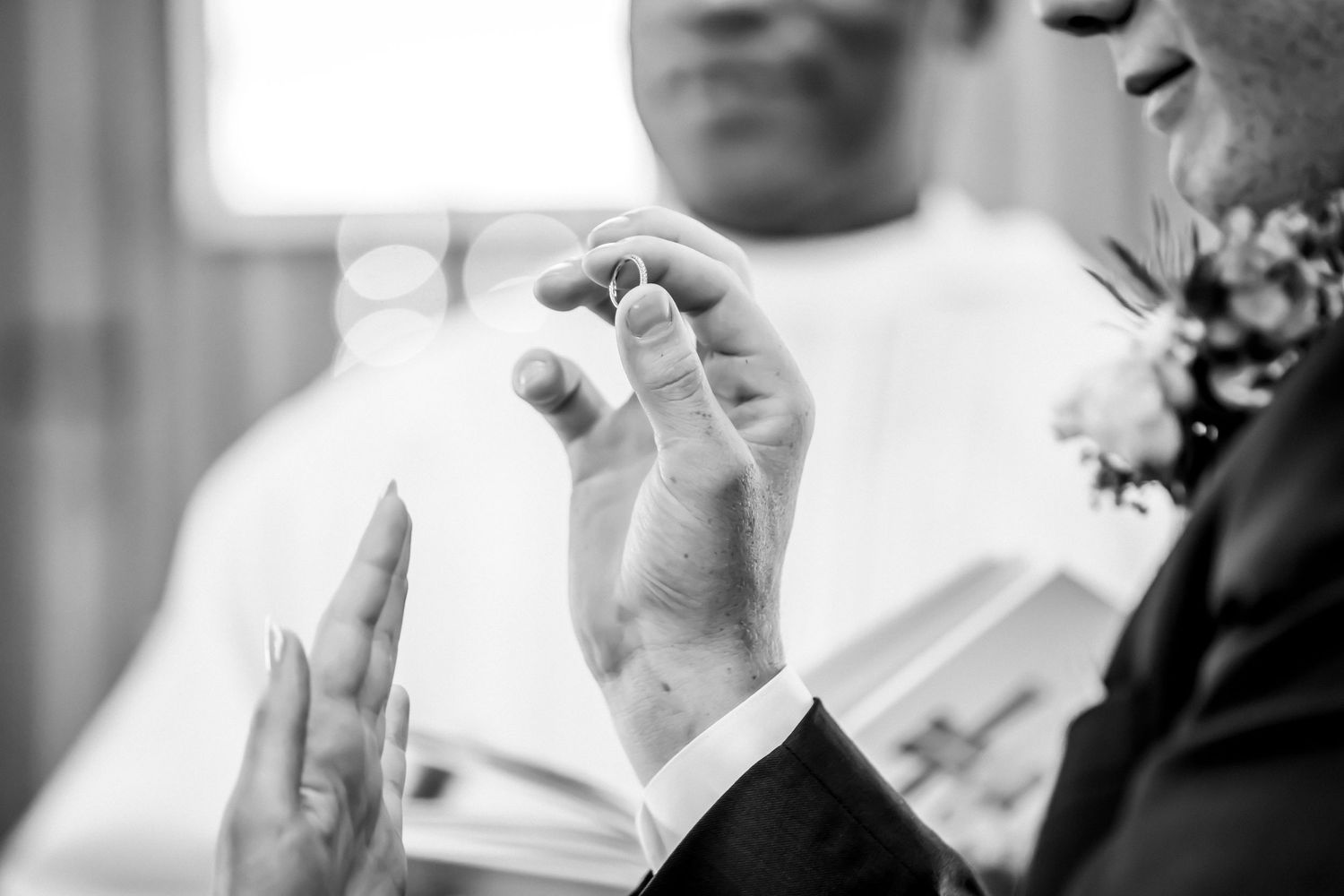 Black and white photo of a groom holding wedding rings during a ceremony.