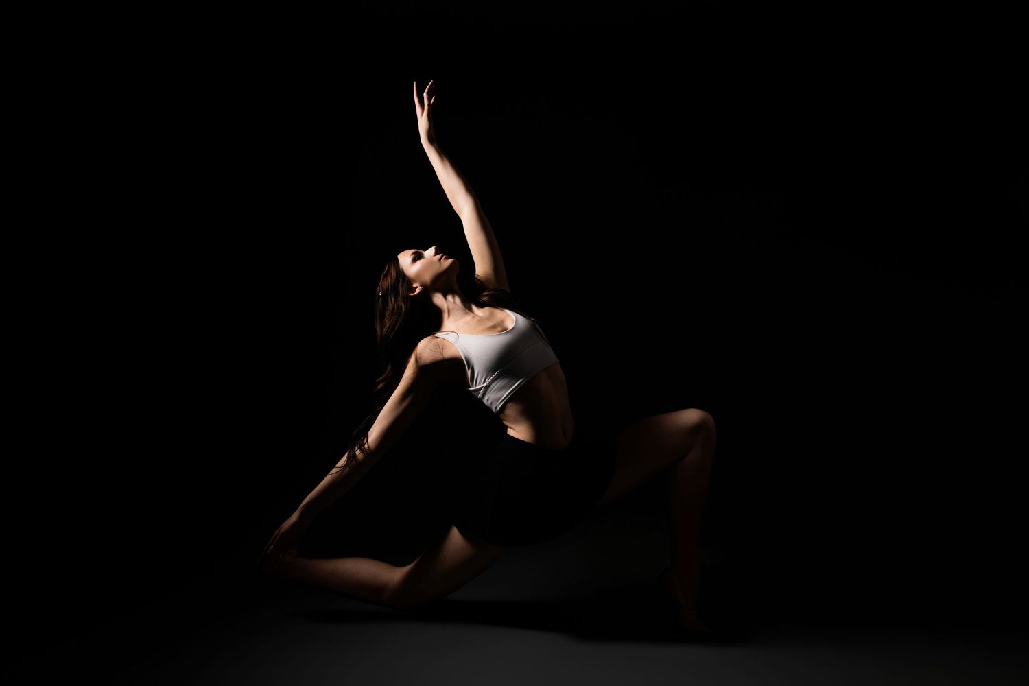 A dancer performs an elegant backbend pose in dramatic studio lighting against a dark background.