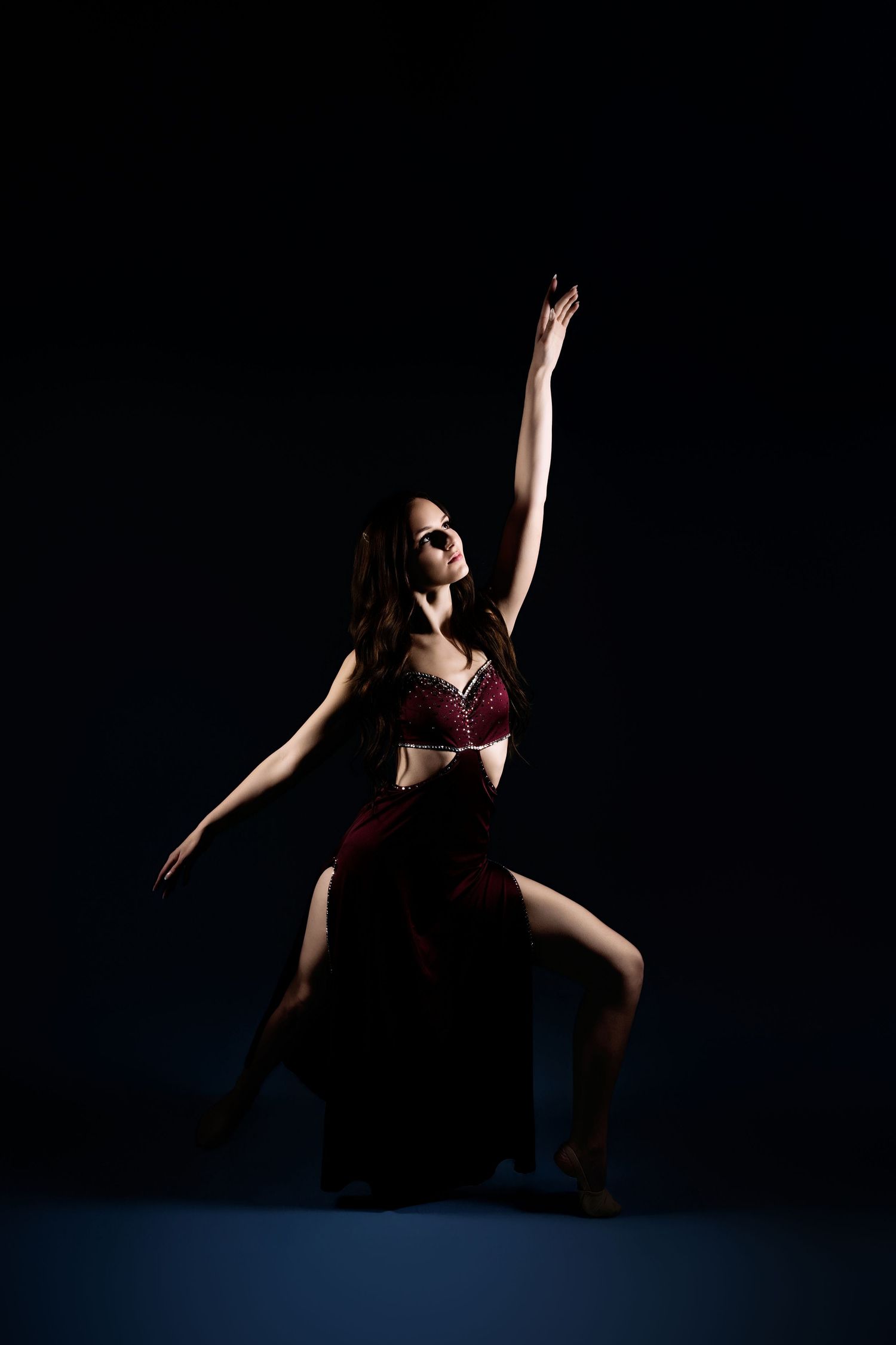 A woman in a red belly dance costume performs an elegant pose with one arm raised against a dark background.