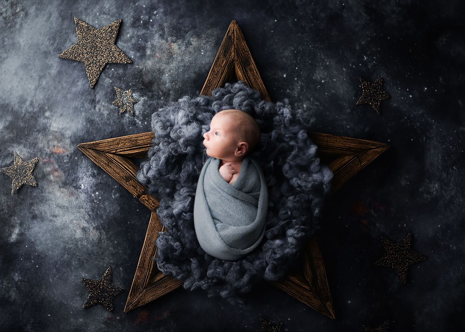 Newborn baby wrapped in gray swaddle nestled in wooden star prop with fluffy blue wool and glittery star decorations.