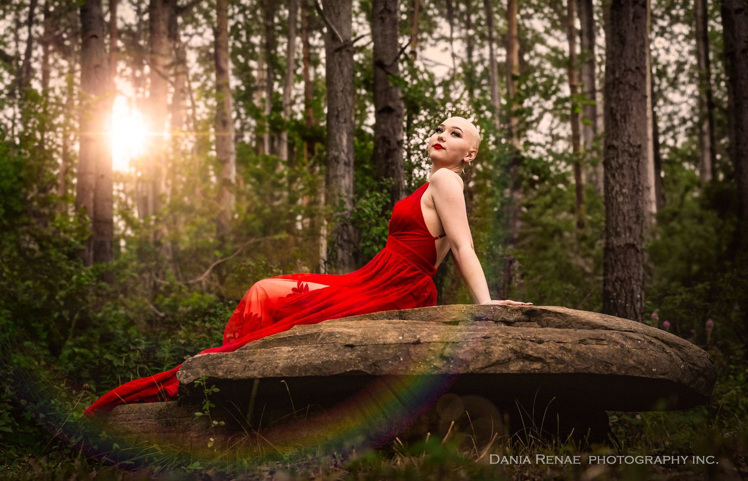 Woman in red gown poses on forest rock at golden sunset, captured by Diana Renae Photography Inc.