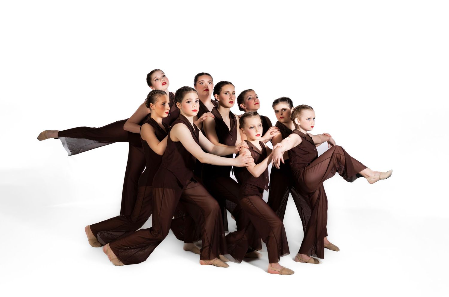 Group of dancers in brown costumes striking a dramatic pose together against a white background.