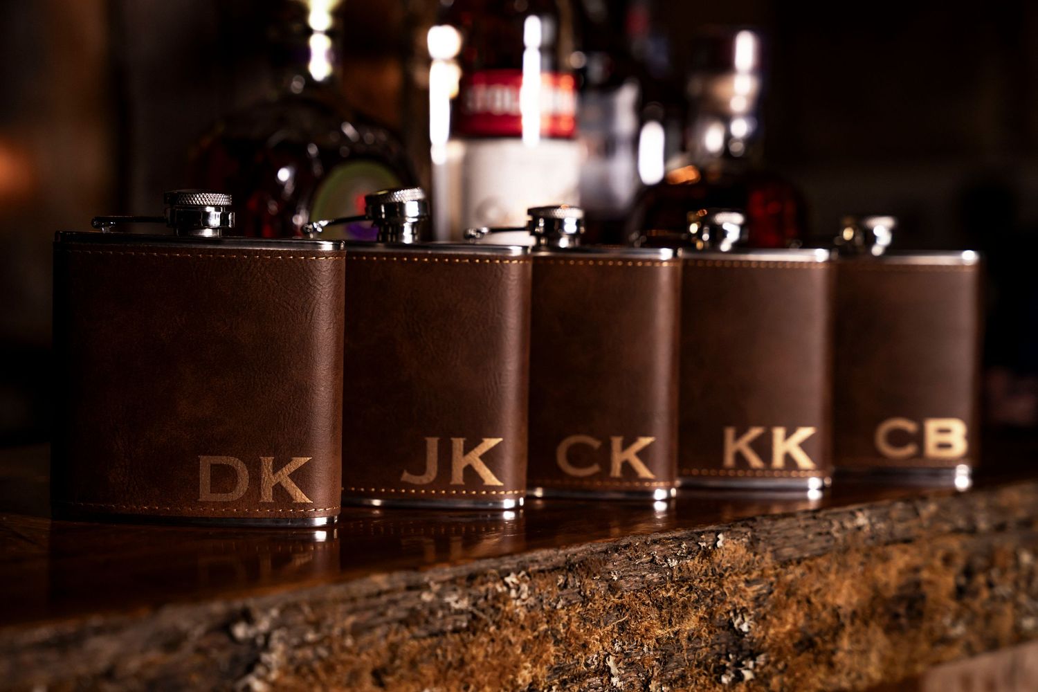 Five personalized brown leather flasks with gold monograms DK, JK, CK, KK, CB, perfect groomsmen gifts.