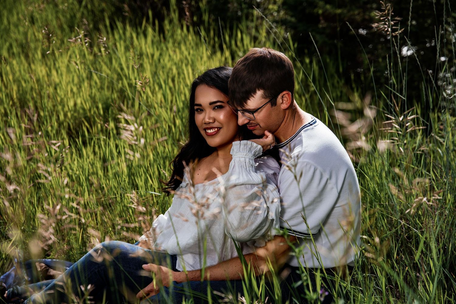 A couple sits together in a lush green meadow, sharing a tender romantic moment among tall grasses.