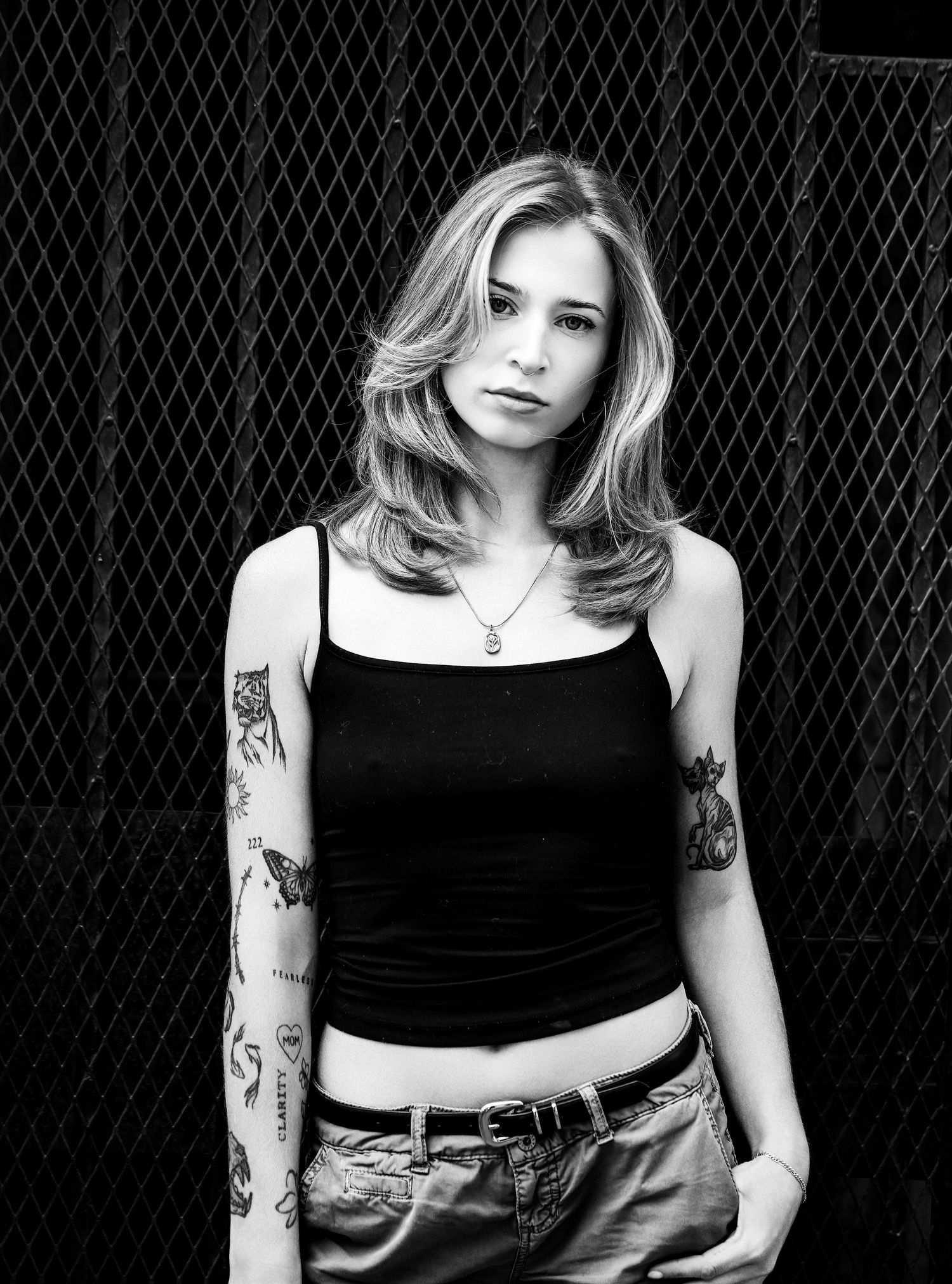 Black and white portrait of a young blonde woman with tattoos wearing a black crop top and jeans.