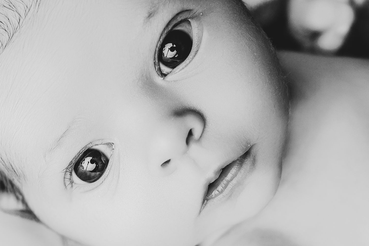 Close-up black and white portrait of a newborn baby with big dark eyes and soft skin.