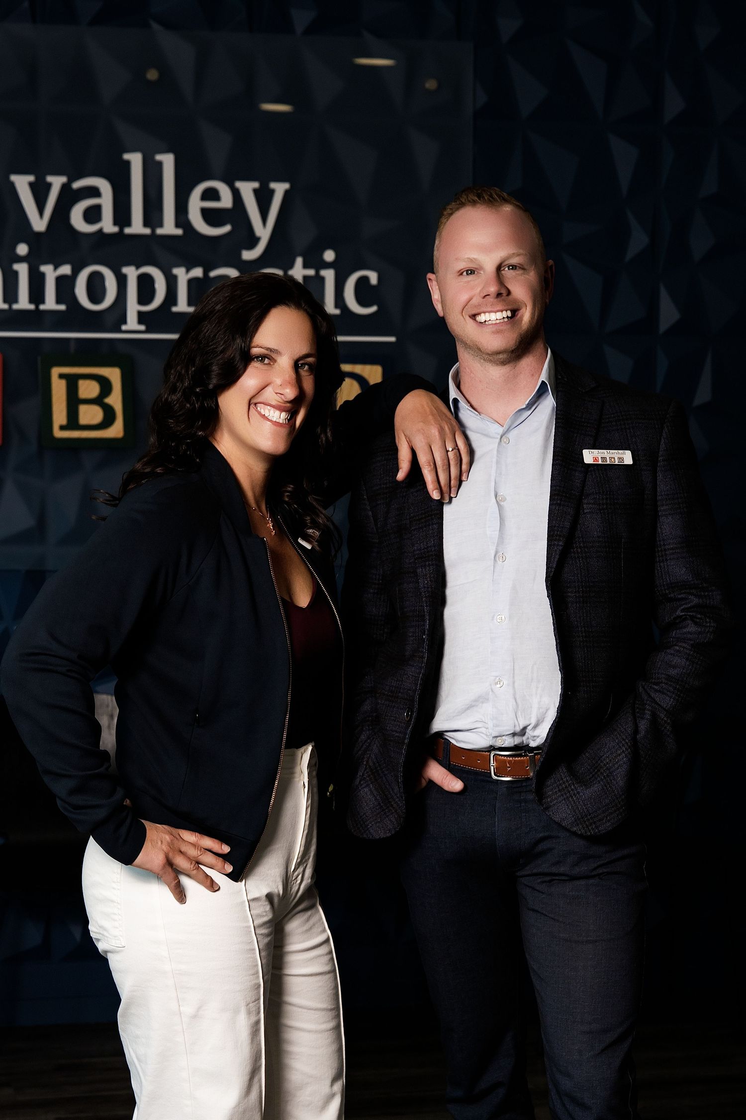 Two professionals smiling in front of a Valley Chiropractic sign at a business event.