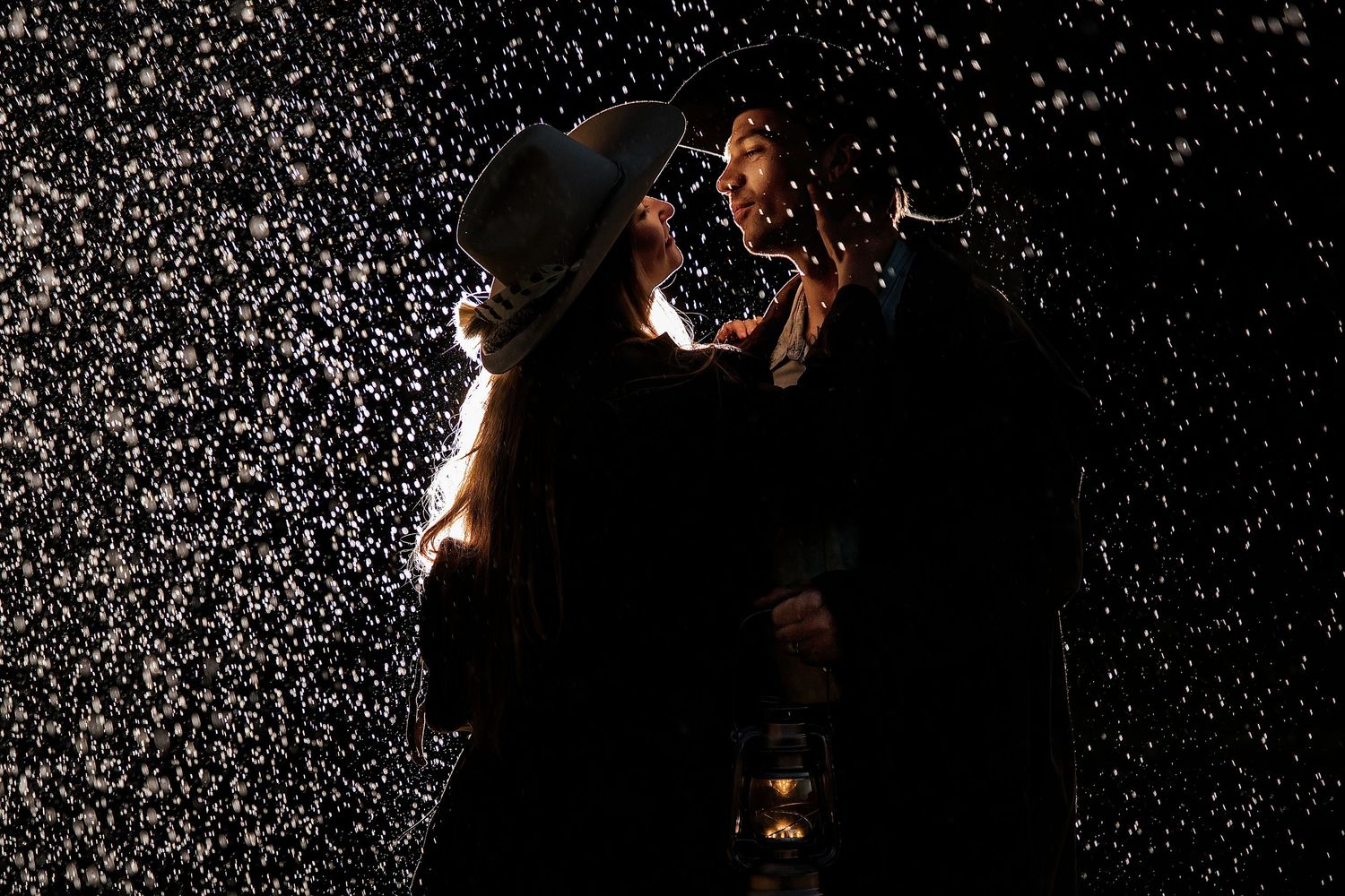 Two people sharing a romantic moment in falling snow at night, illuminated by a warm lantern glow.