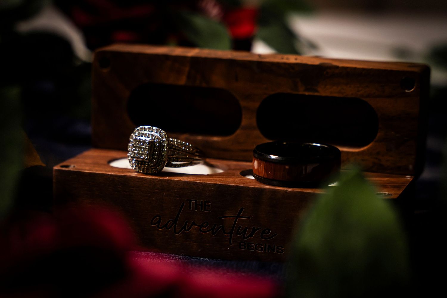Close-up of diamond engagement ring and wooden wedding band displayed in a rustic wooden ring box.