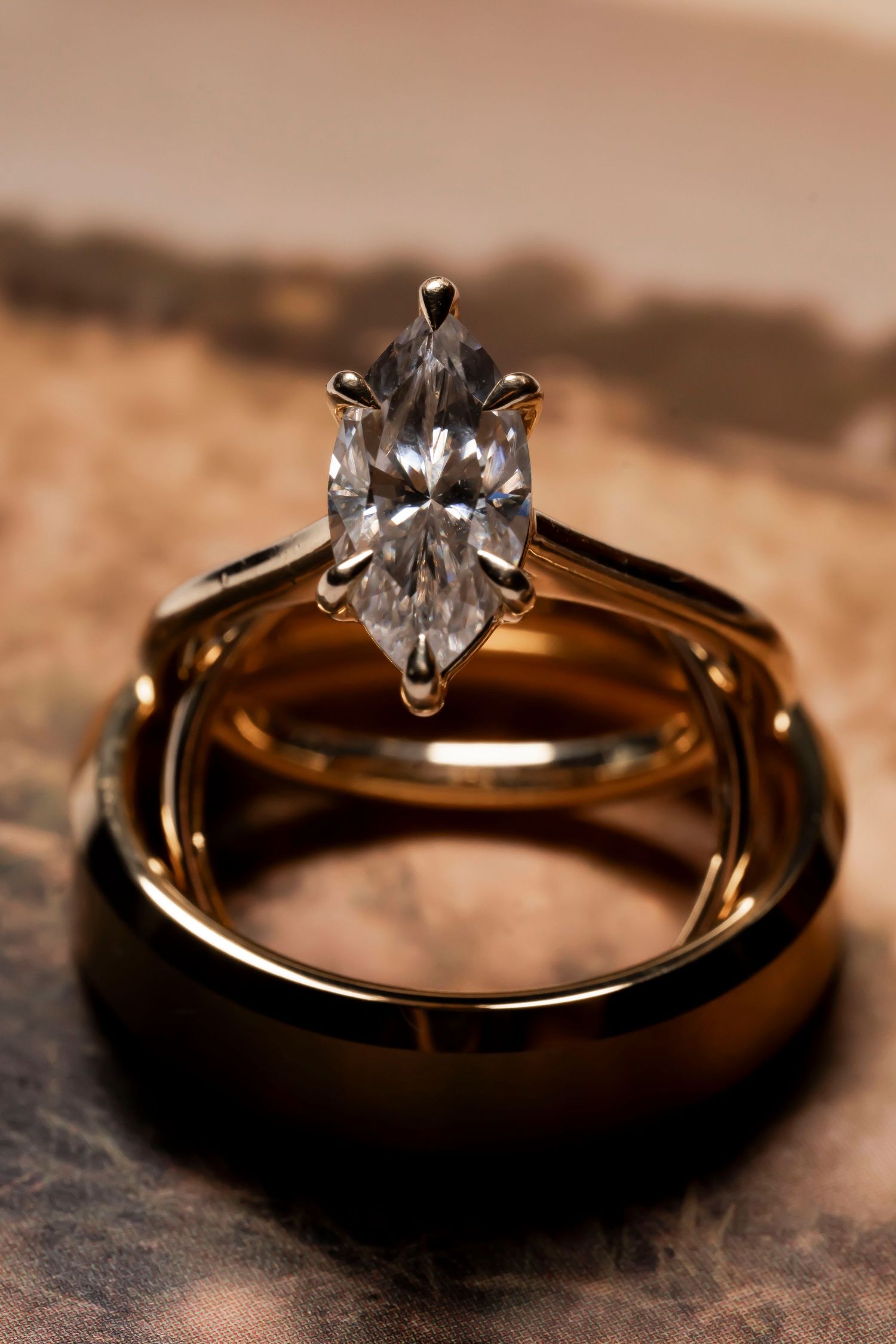 Gold wedding band and marquise diamond solitaire engagement ring stacked together on a leather surface.