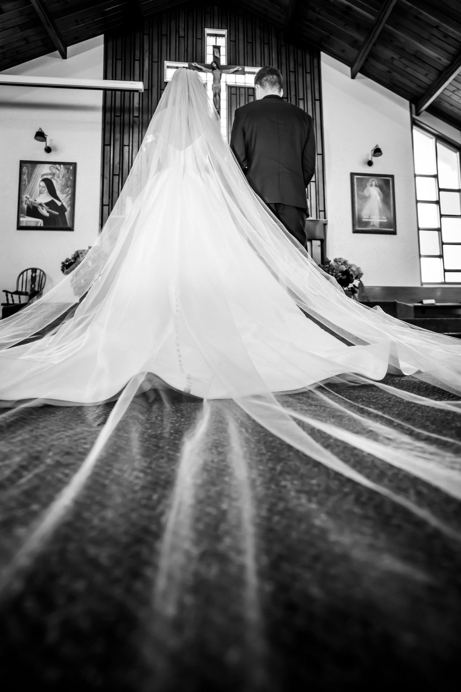 Black and white photo of a bride and groom at the altar, her long veil trailing down the church aisle.