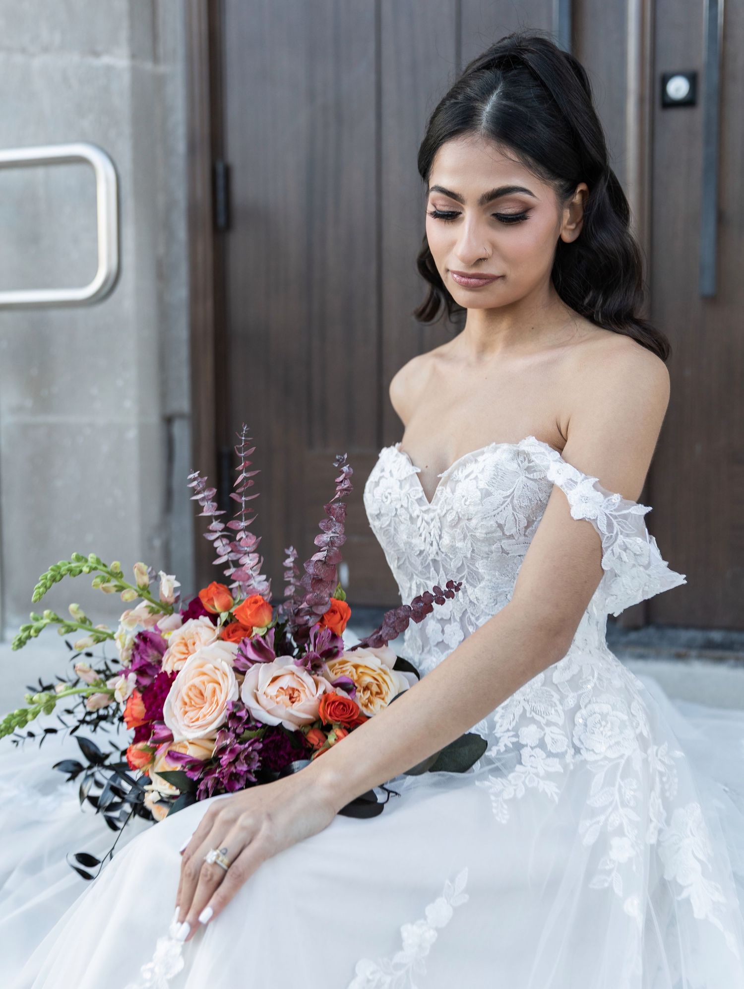 Bride in off-shoulder lace ball gown holding a vibrant bouquet of orange, pink, and purple flowers.
