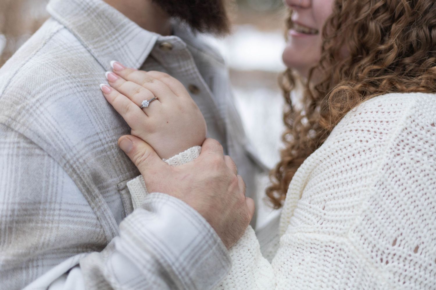 Close-up of a couple embracing, woman wearing an engagement ring, dressed in cozy sweaters.
