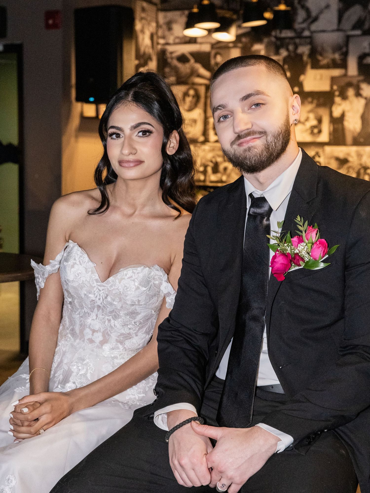 Newlywed couple poses together, bride in lace gown and groom in black suit with pink boutonniere.