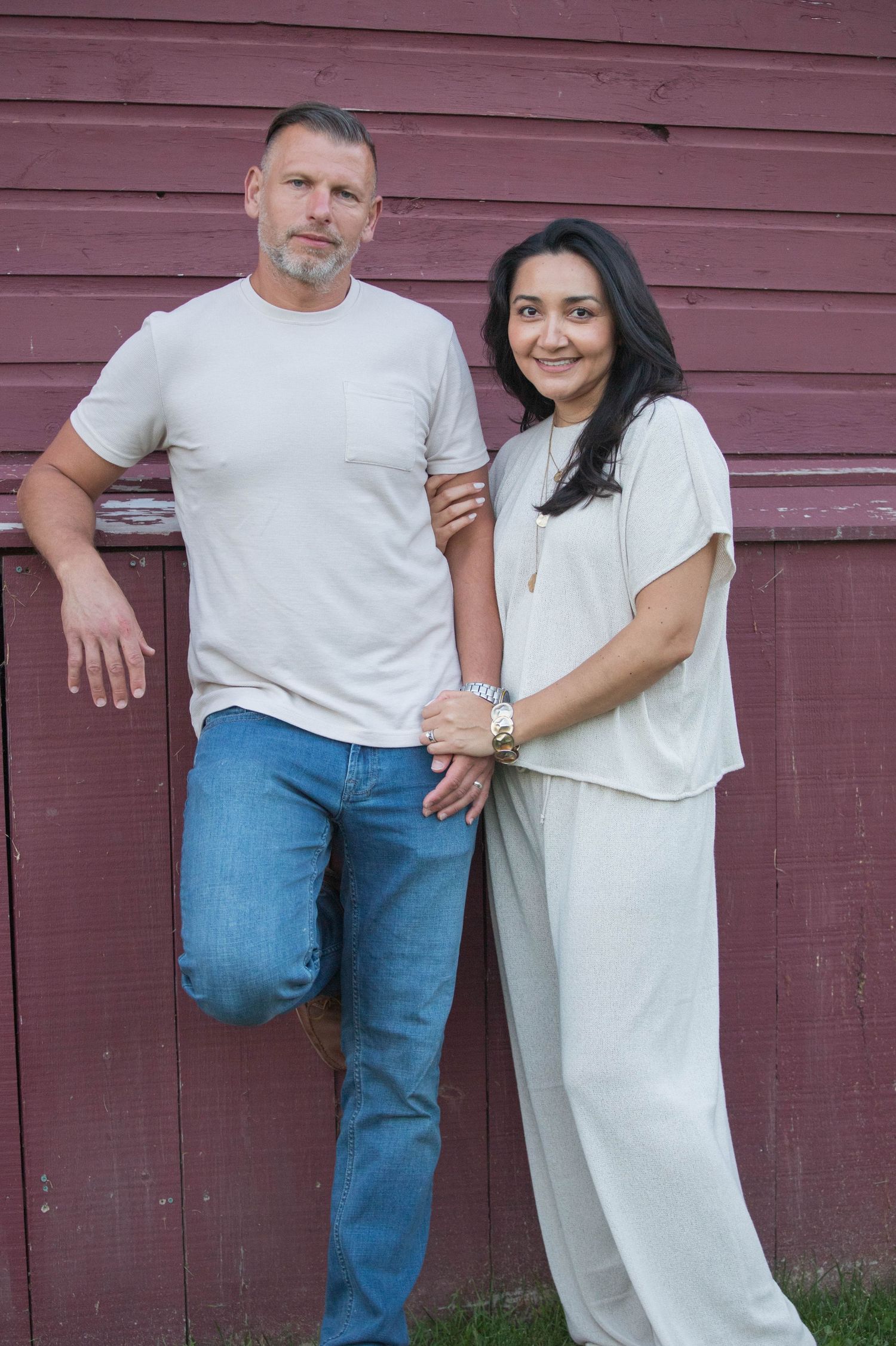 Couple leaning against rustic red barn wall, man in white tee and jeans.
