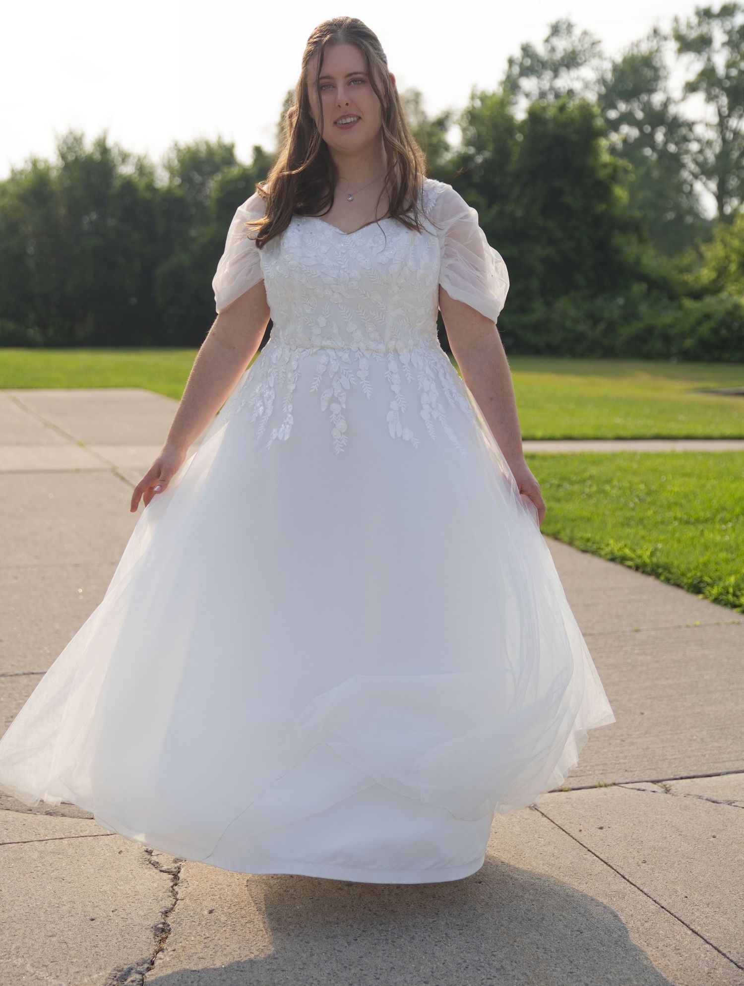 Plus-size bride wearing a white ball gown wedding dress with lace bodice and puff sleeves outdoors.