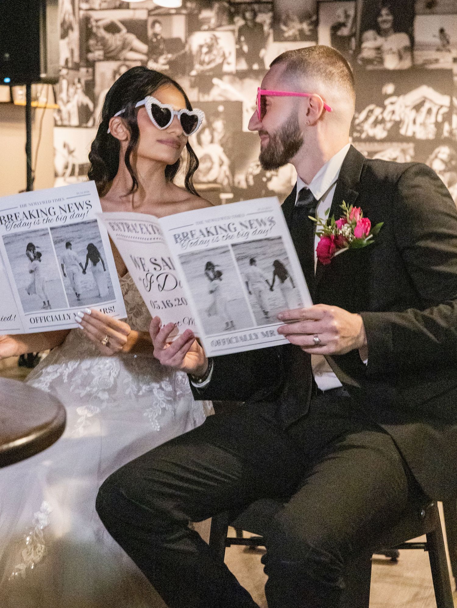Newlyweds in heart-shaped sunglasses playfully read their custom wedding newspaper announcement together.