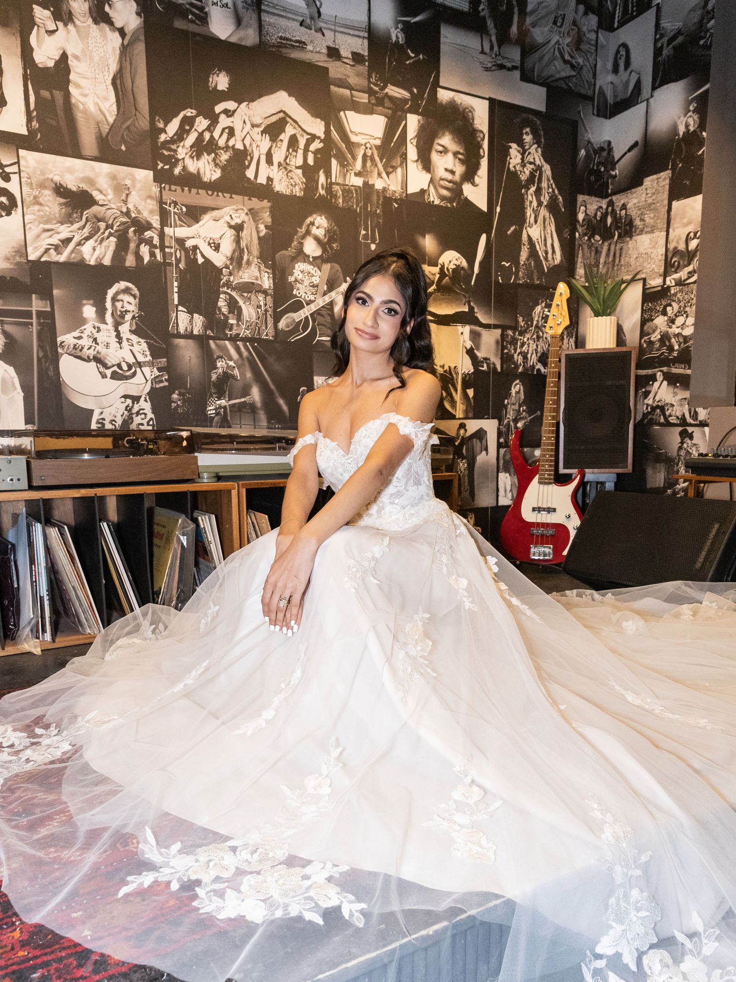 Bride in a floral lace off-shoulder ball gown posing in a music-themed room with rock photography walls.
