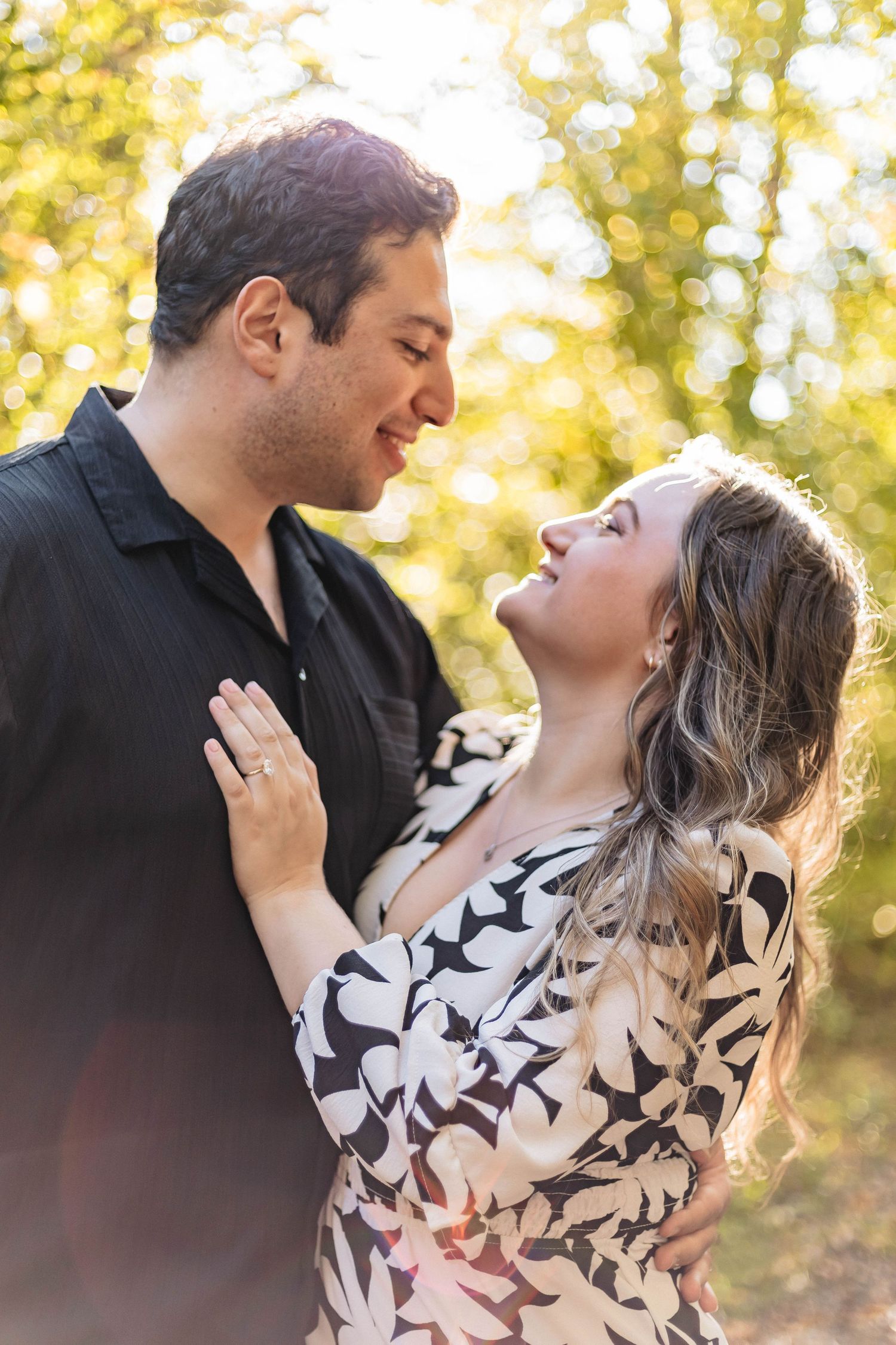 Romantic couple gazing at each other outdoors in golden sunlight during an engagement photo session.
