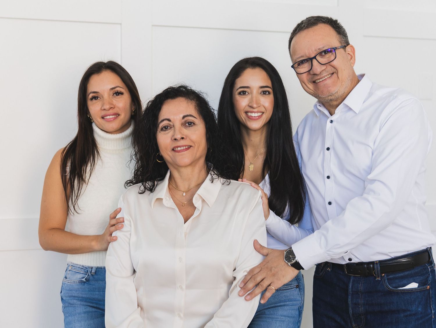 Family of four portrait featuring parents and two adult daughters posing together against a clean white background.