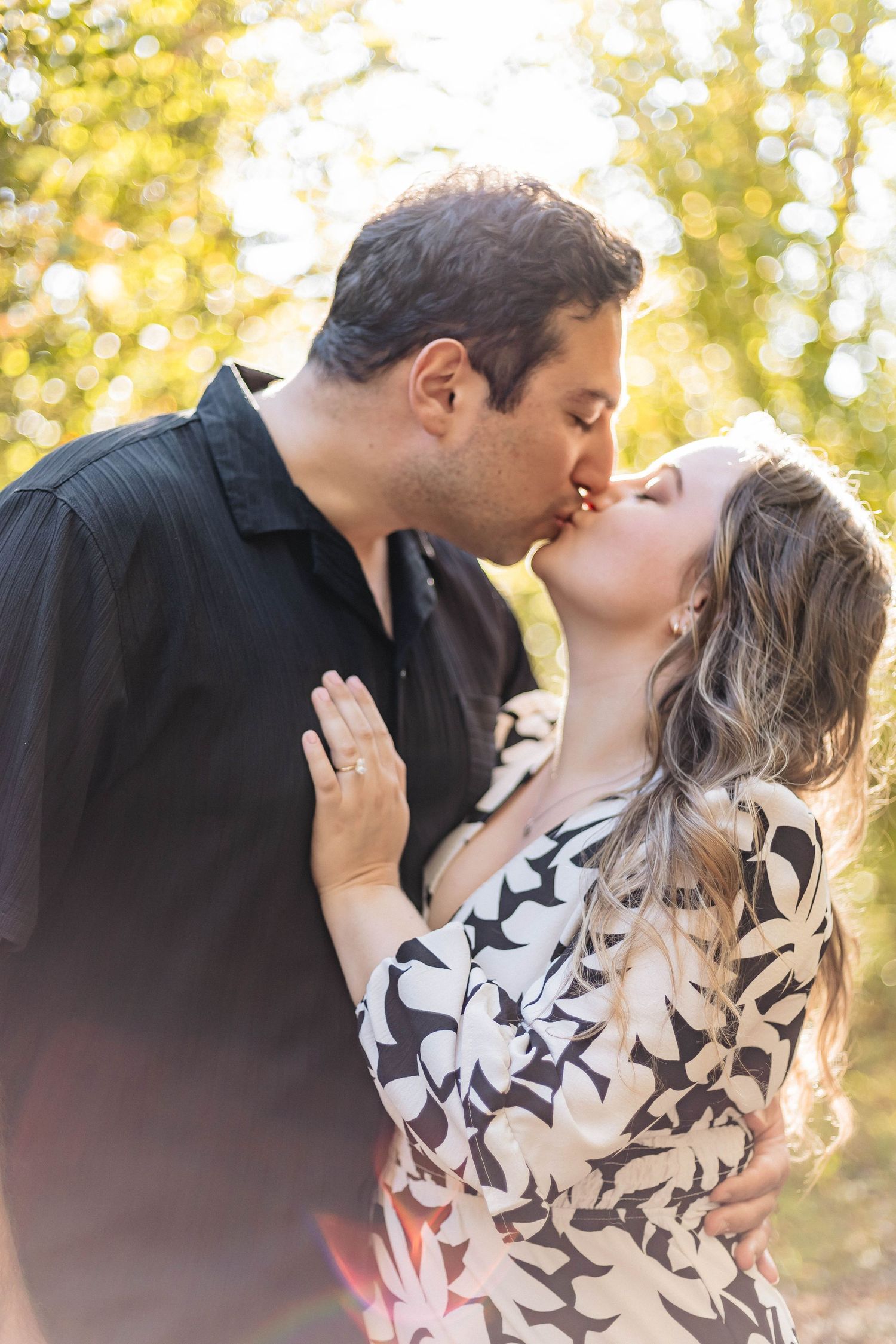 Romantic couple sharing a kiss outdoors with warm golden bokeh sunlight in background.