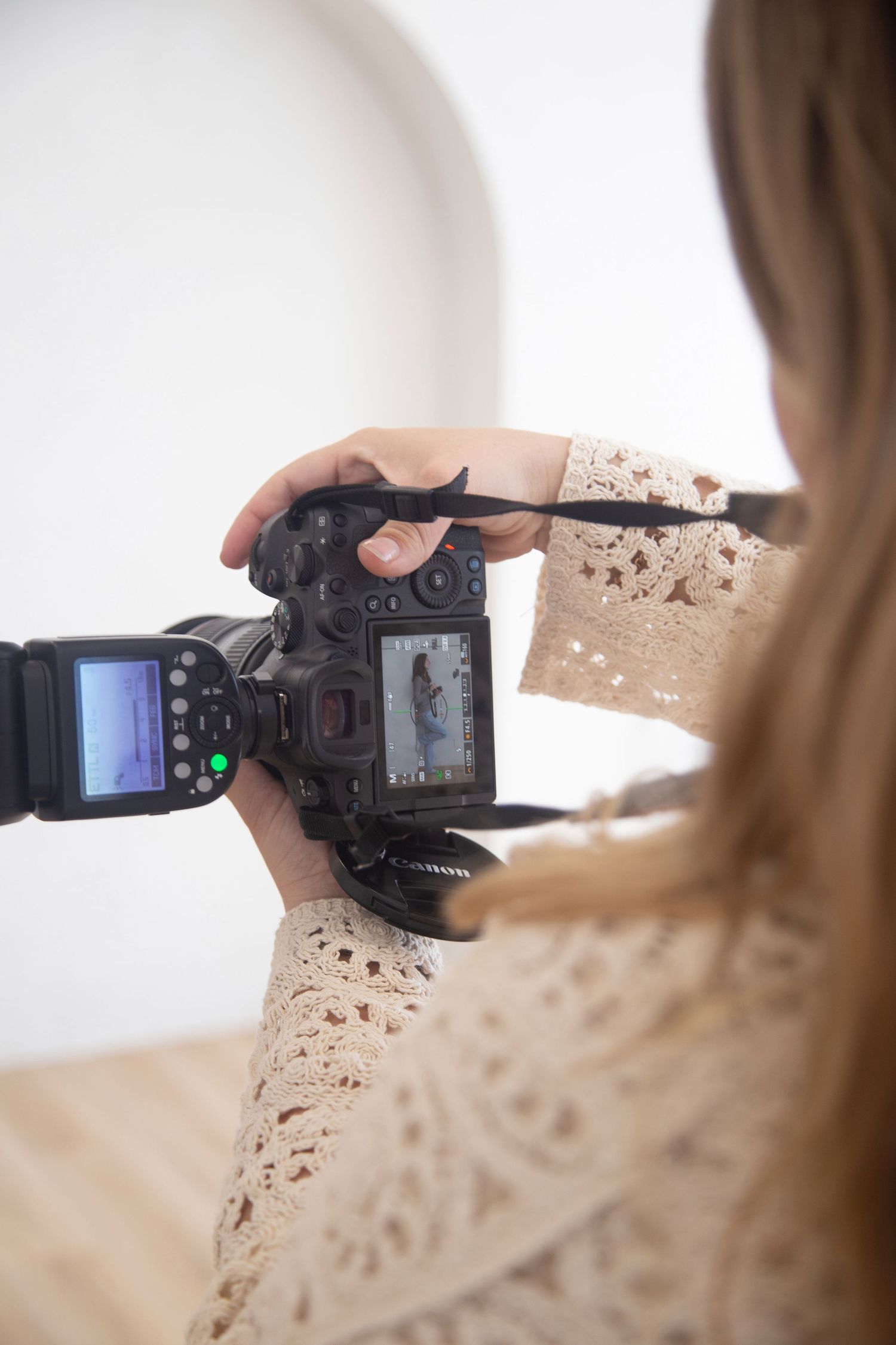A photographer reviews photos on the LCD screen of her DSLR camera while wearing a cream lace top.