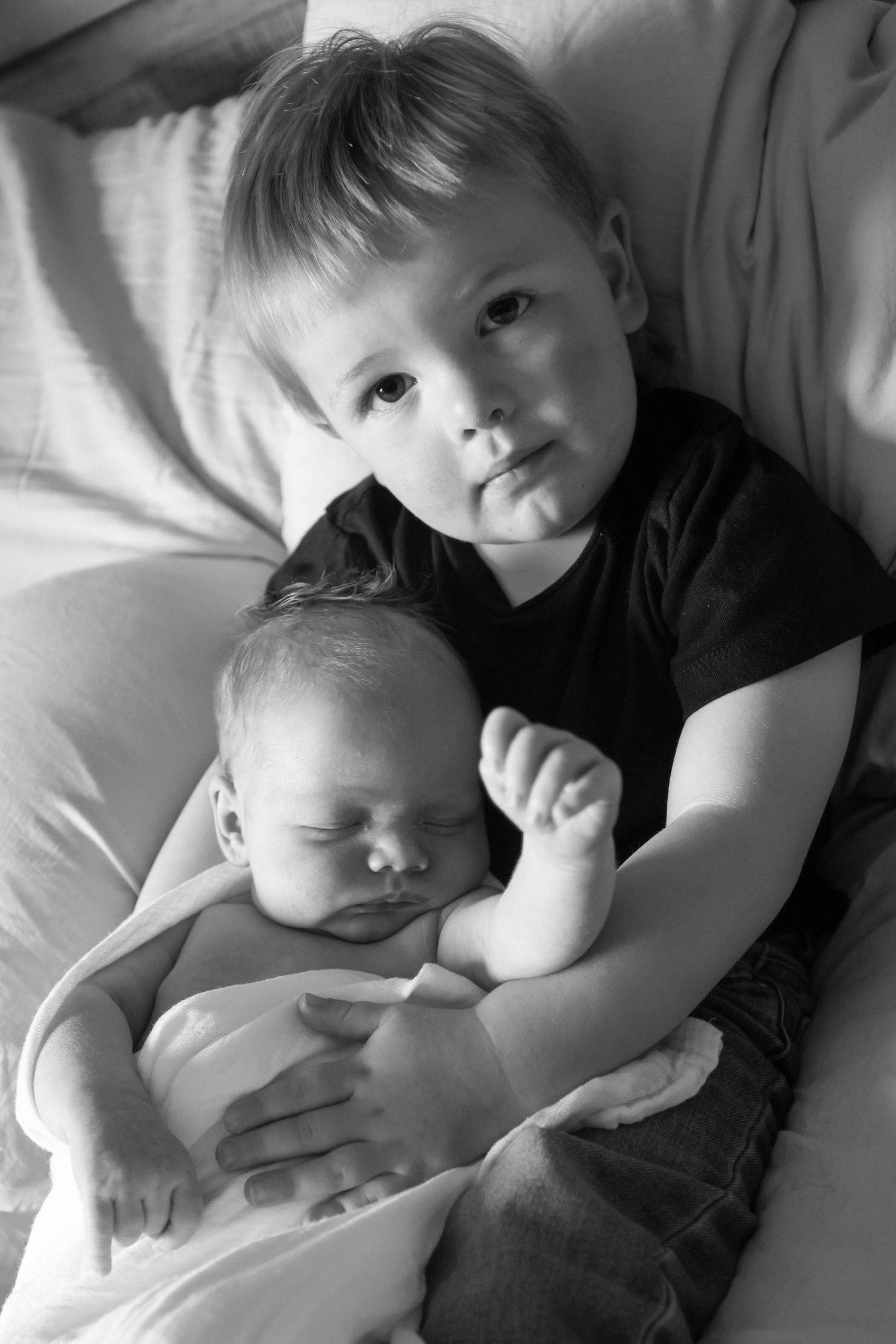 Black and white portrait of young boy tenderly holding sleeping newborn baby sibling.