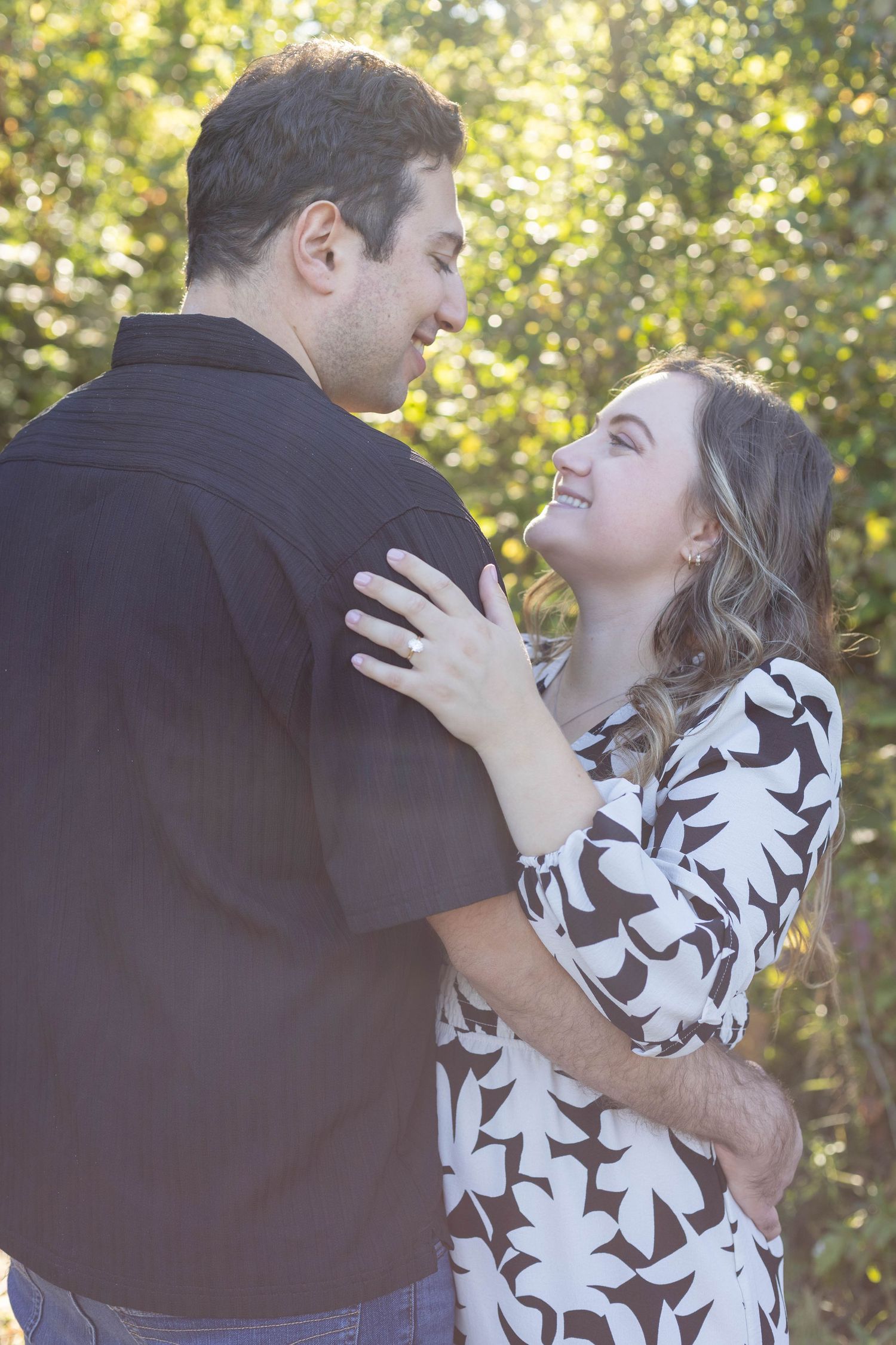 Happy couple embracing and smiling at each other outdoors surrounded by green foliage.