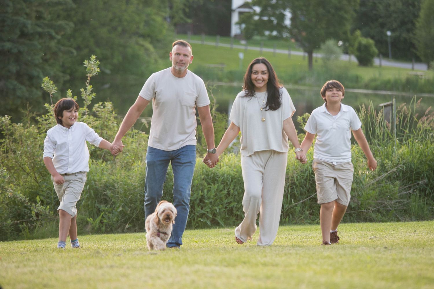 Happy family with dog walking together on green grass in sunny outdoor park setting.