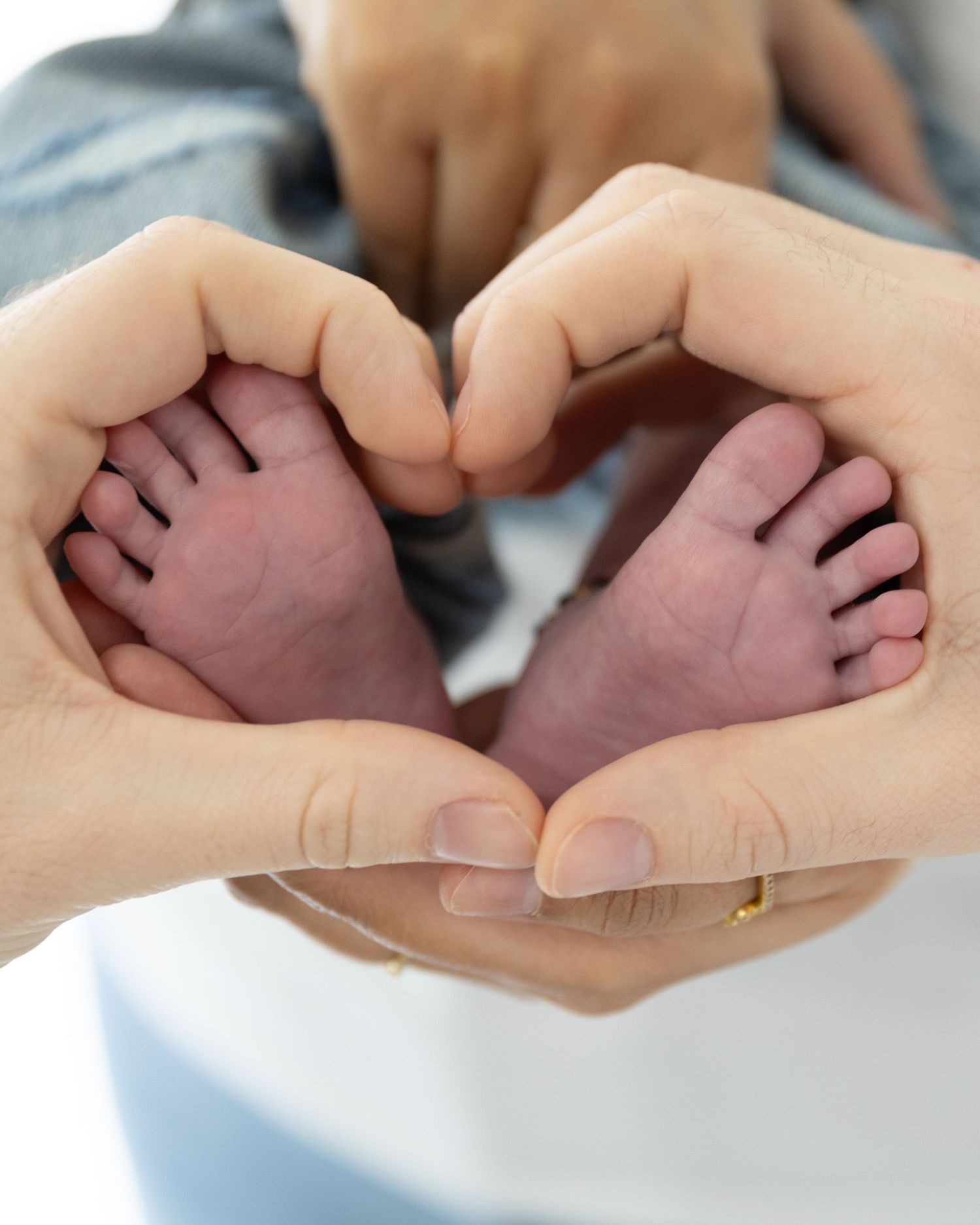 Adult hands forming a heart shape around tiny newborn baby feet, symbolizing love and new parenthood.