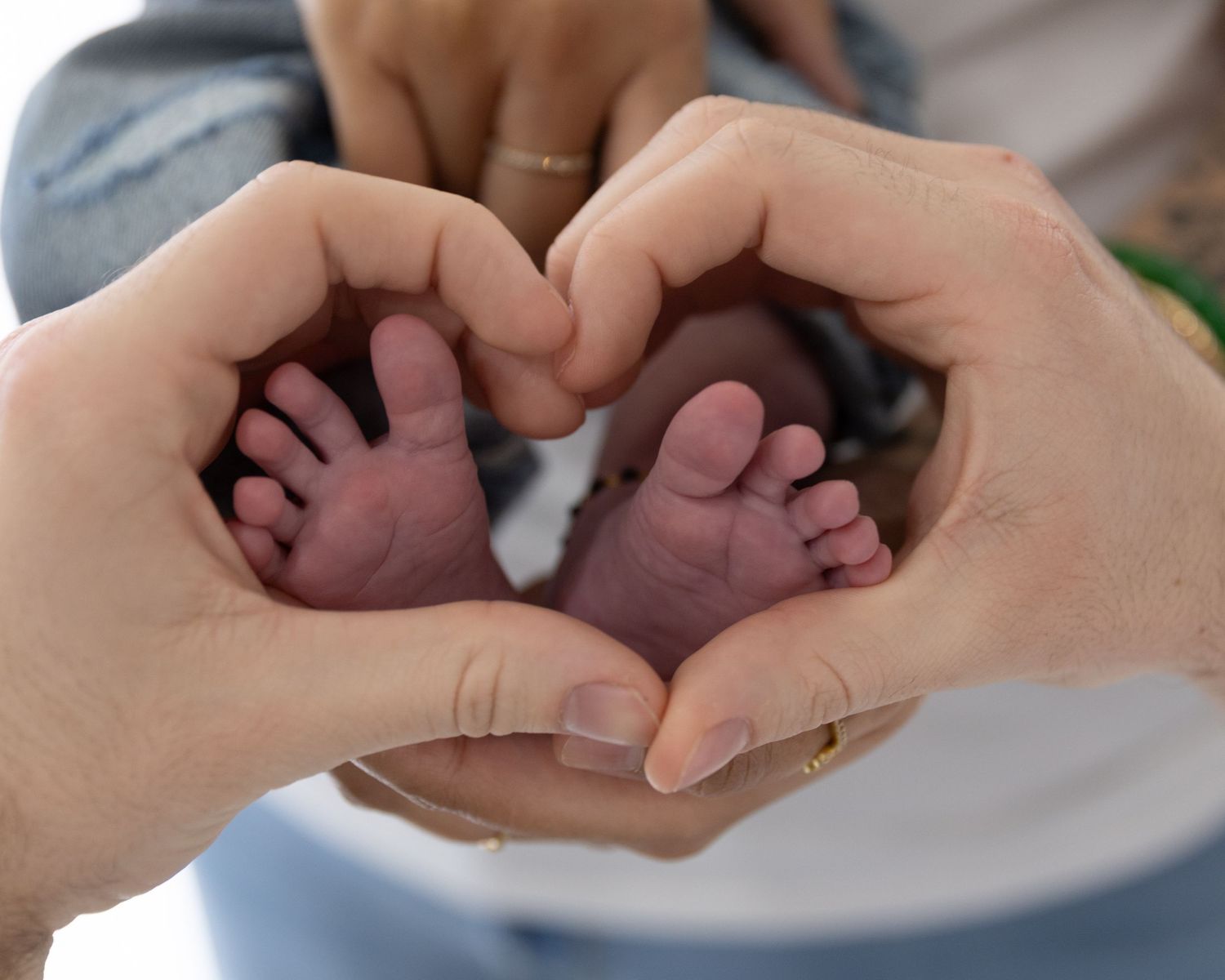 Two hands forming a heart shape around tiny newborn baby feet, symbolizing parental love and new life.
