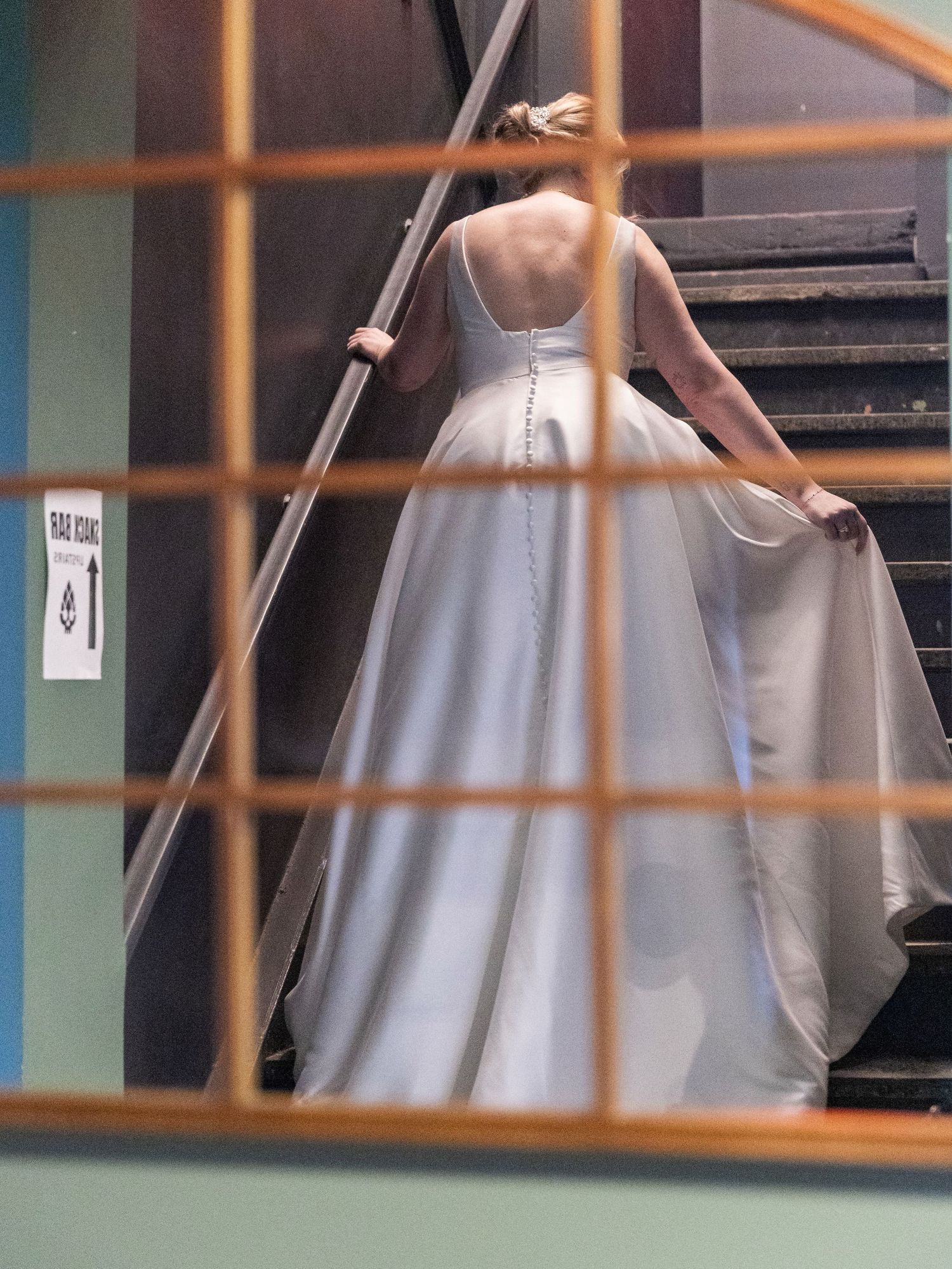 Bride in white satin ball gown with button back detail climbing stairs in venue.
